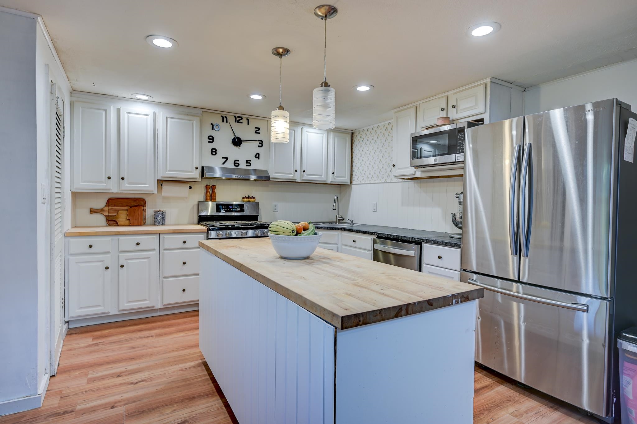Kitchen with white cabinets, stainless steel appliances, and a butcher-block island with a fruit bowl.