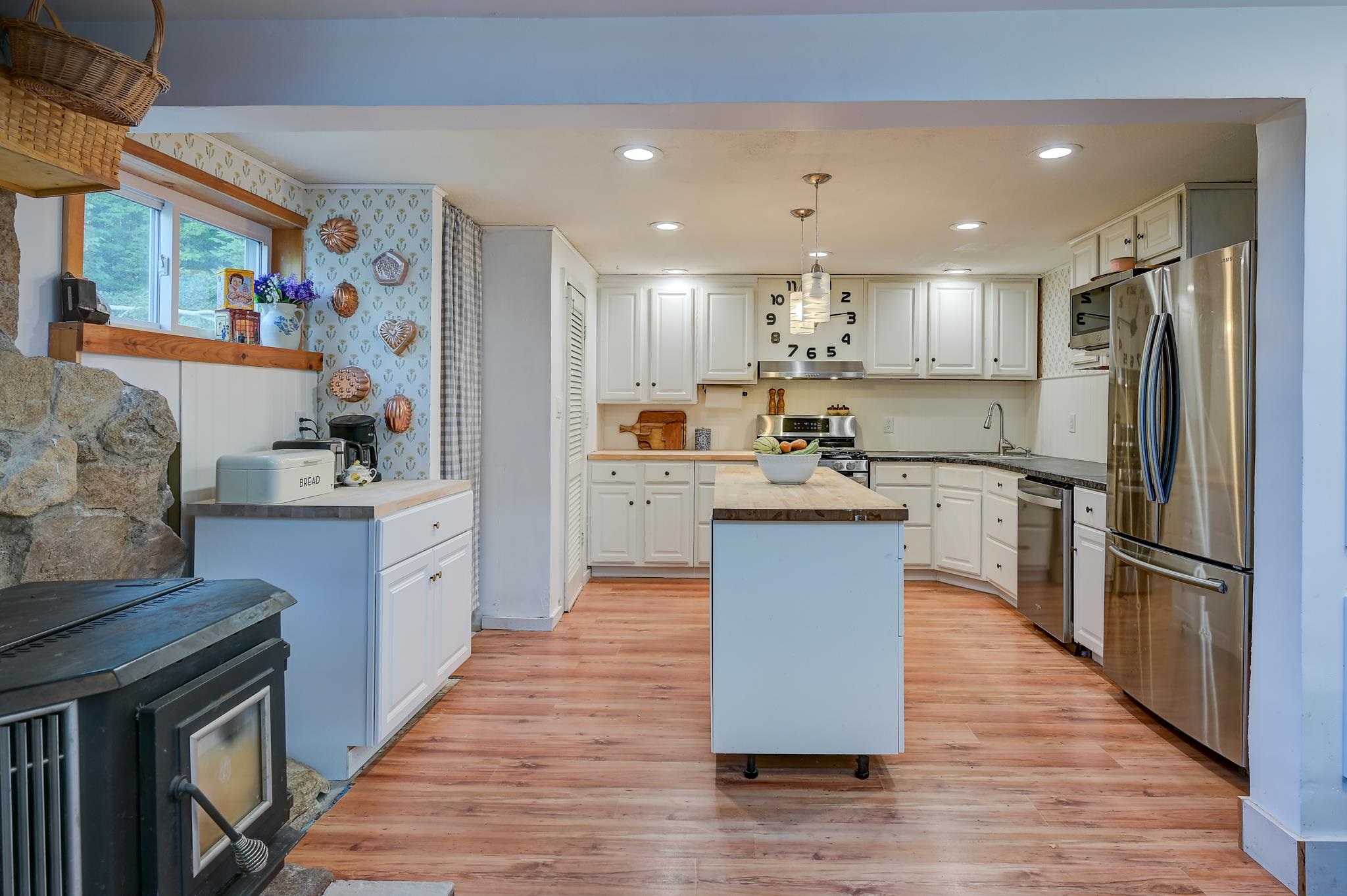 Kitchen with a central island, white cabinets, stainless appliances, and a wood stove beside a stone wall.