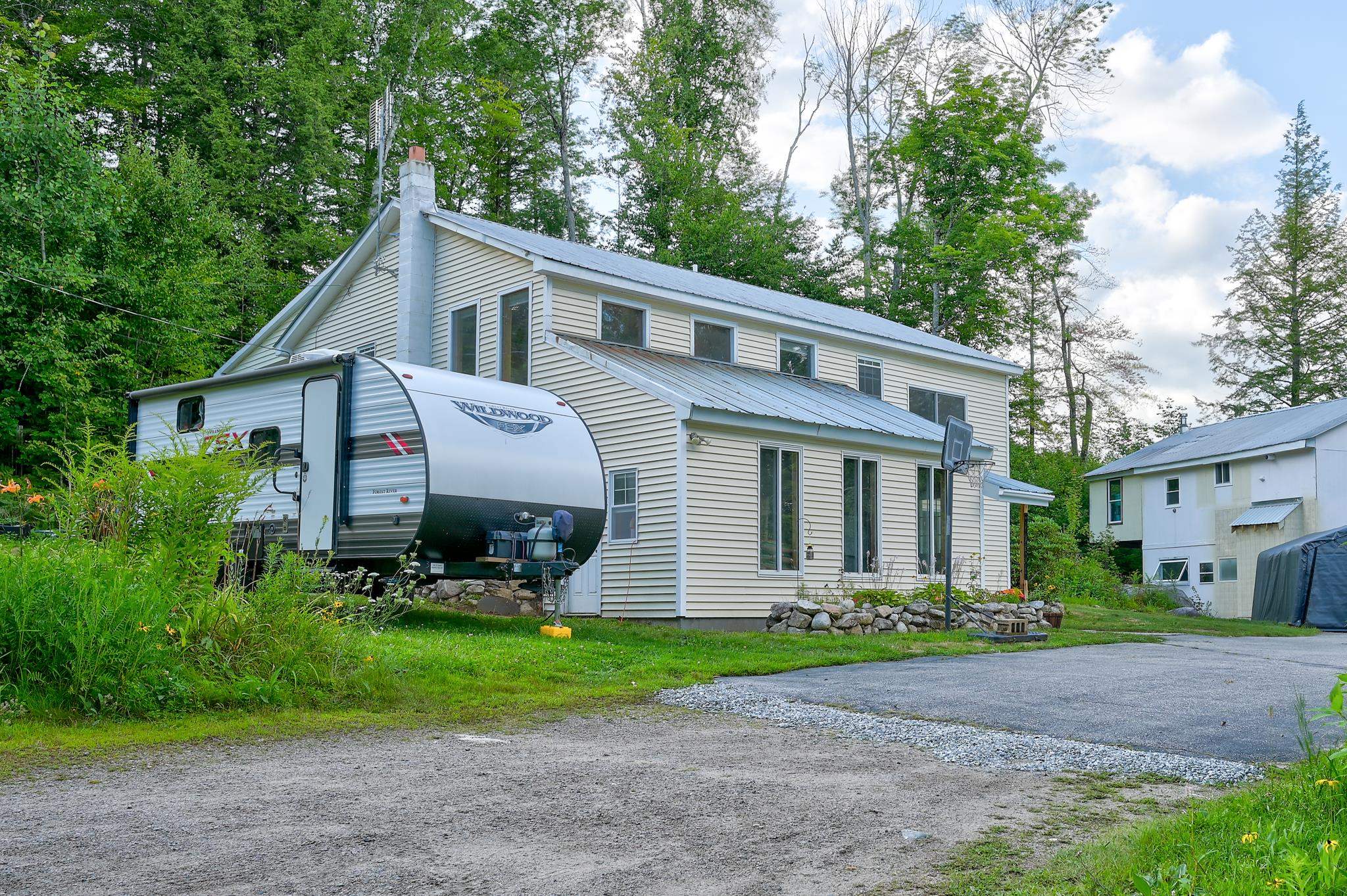 Light-colored two-story house with a metal roof, a travel trailer beside it, and a white outbuilding nearby.