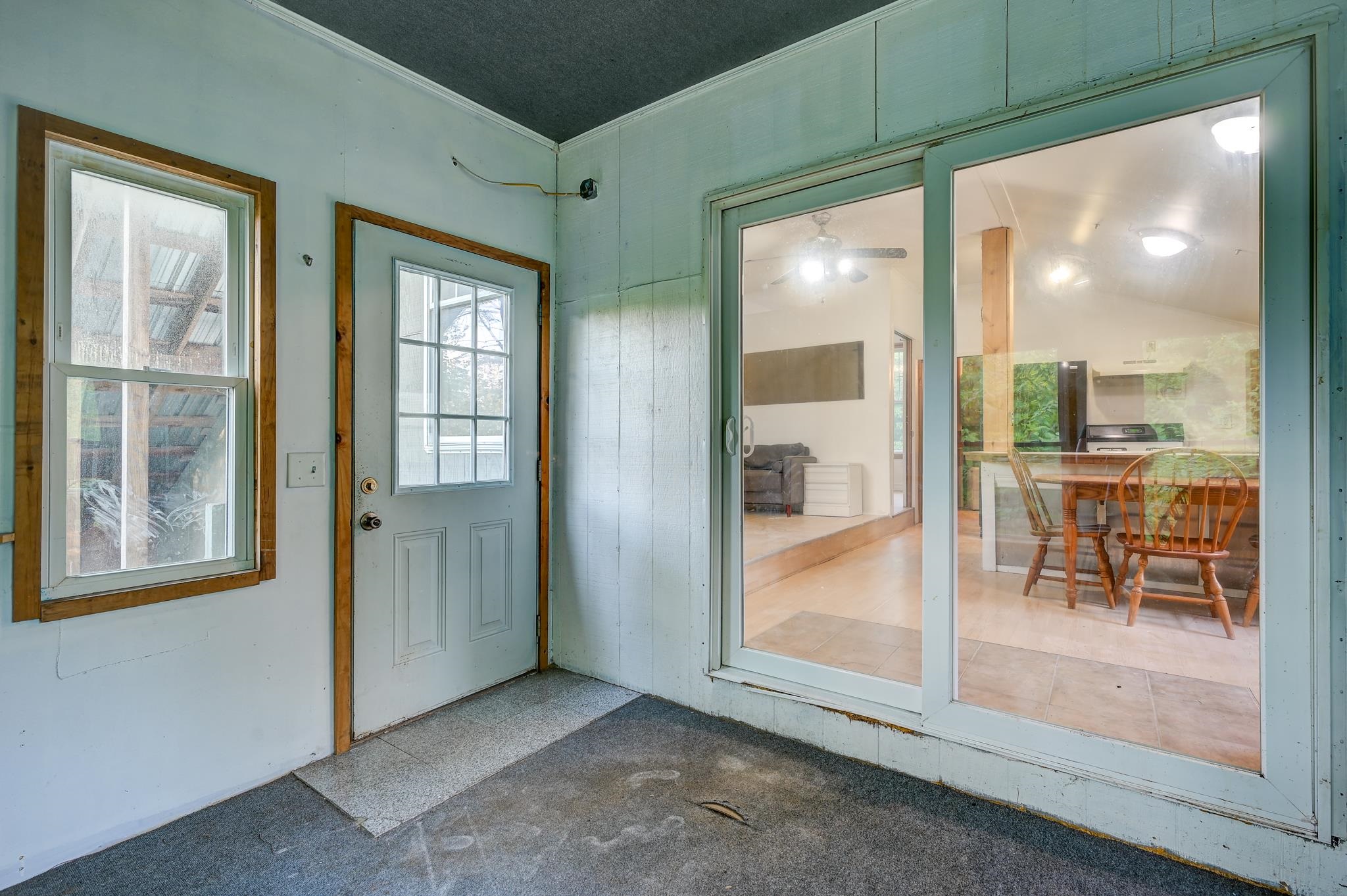 Enclosed porch with a gray entry door and sliding glass doors opening onto a dining and living area.