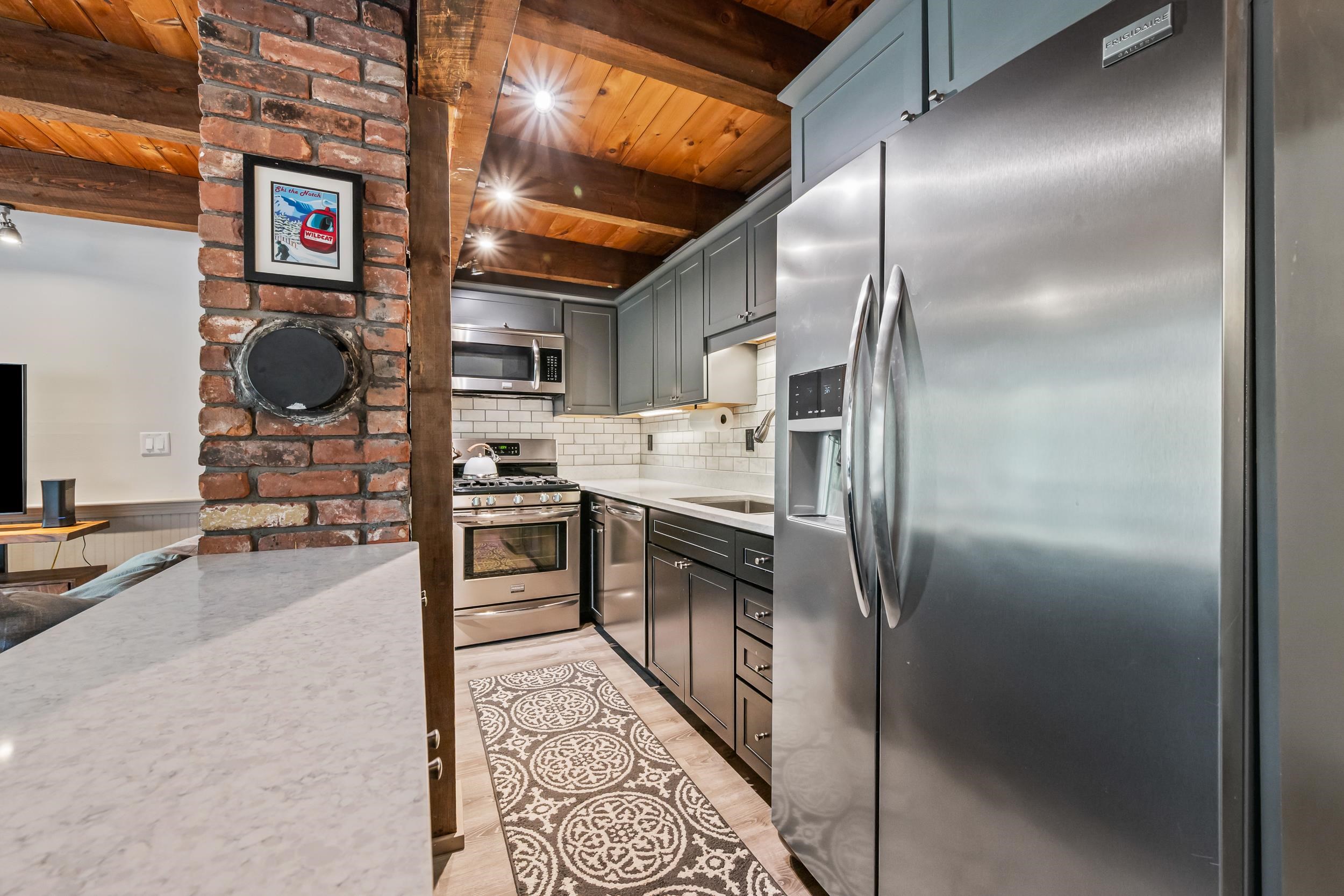 Kitchen with gray cabinets, stainless steel appliances, exposed wood ceiling beams, and a brick column.