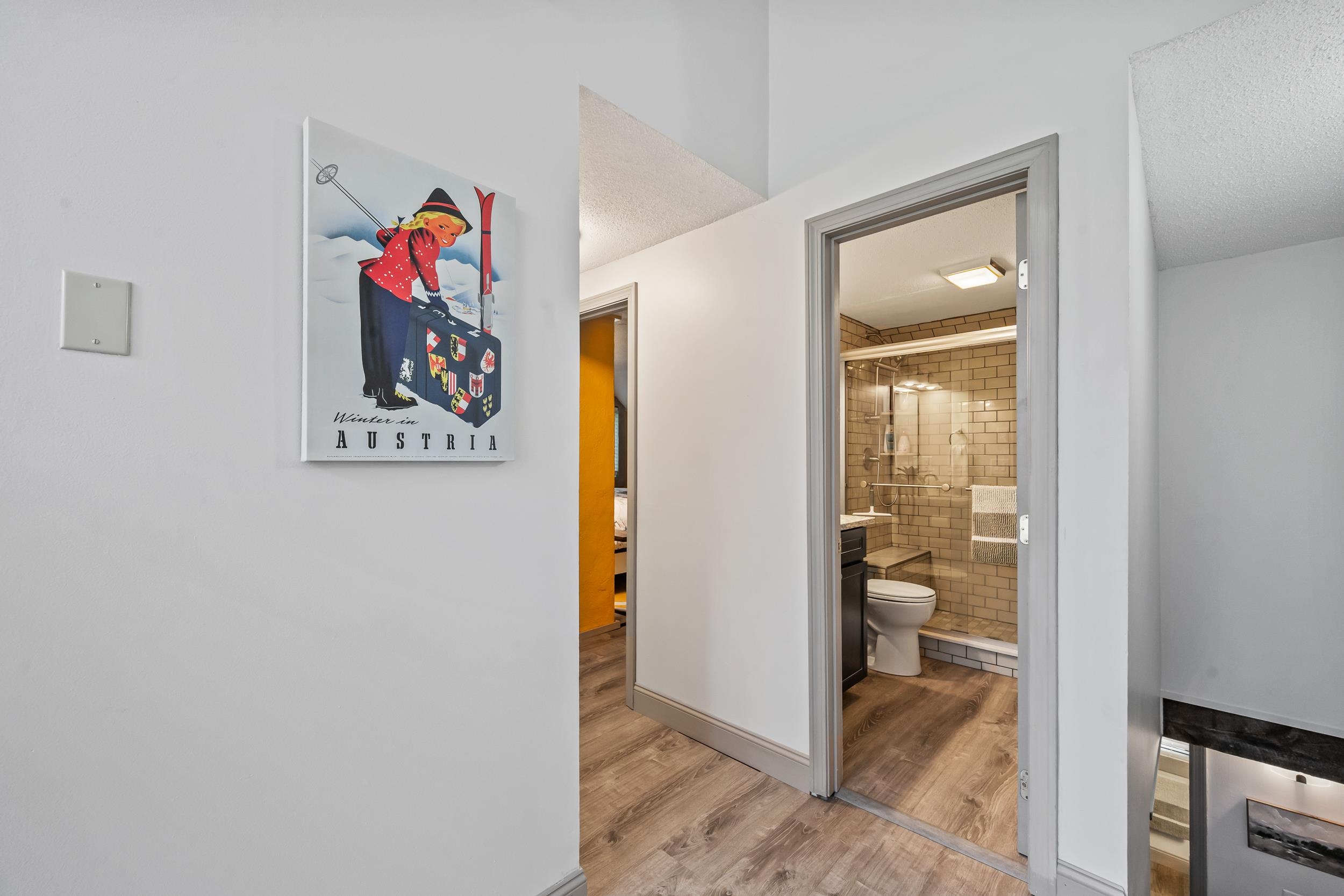 Hallway opening onto a tiled bathroom with a walk-in shower and vintage ski poster.