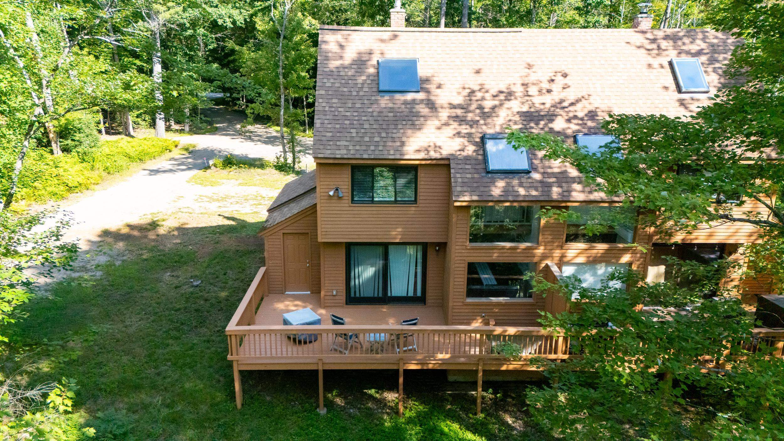 Brown multi-level townhouse with a raised deck and outdoor chairs, surrounded by mature trees.