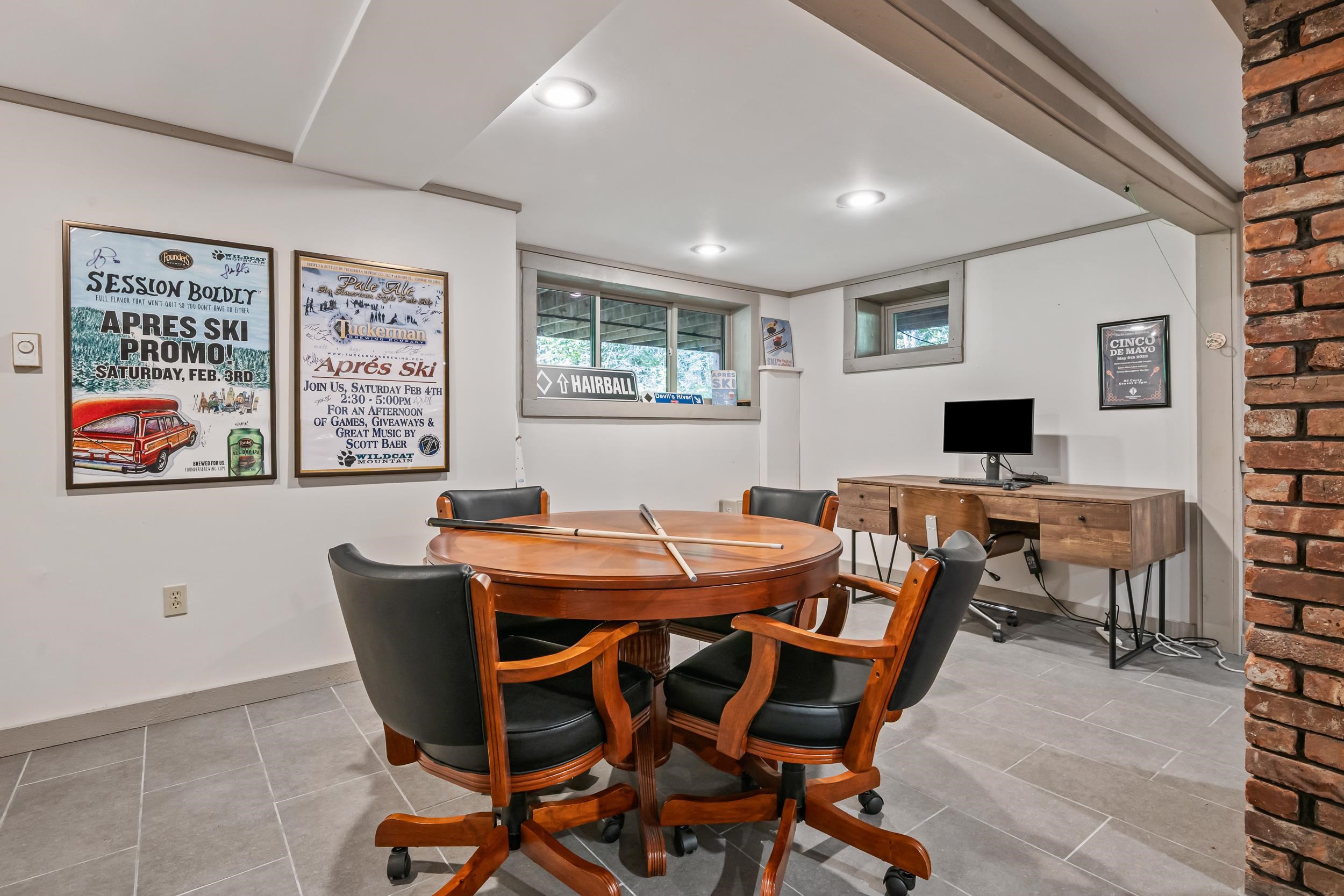 Furnished recreation room with a round table, pool cues, ski posters, and a desk.