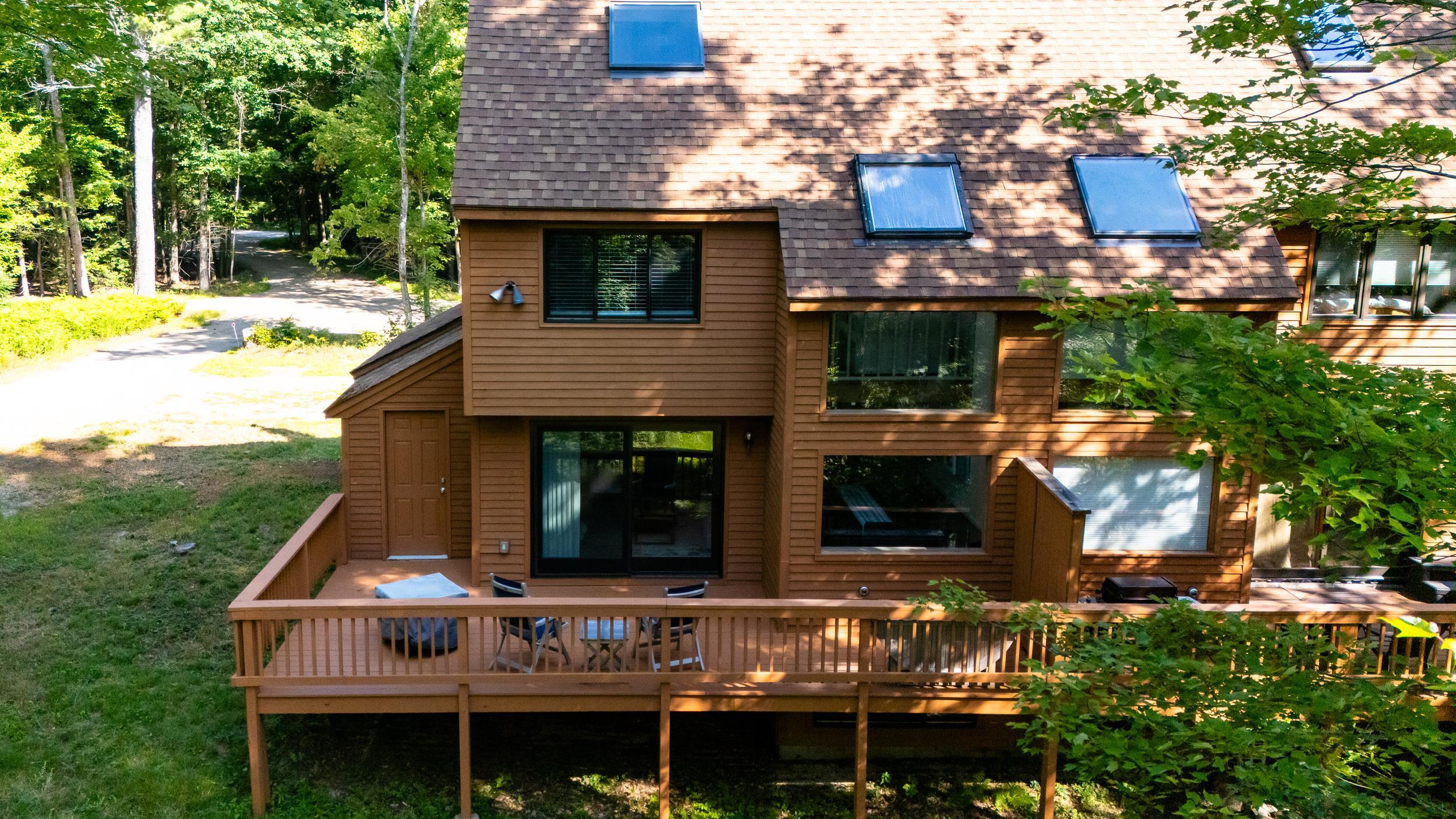 Brown multi-level home with skylights and a large raised deck among leafy trees.