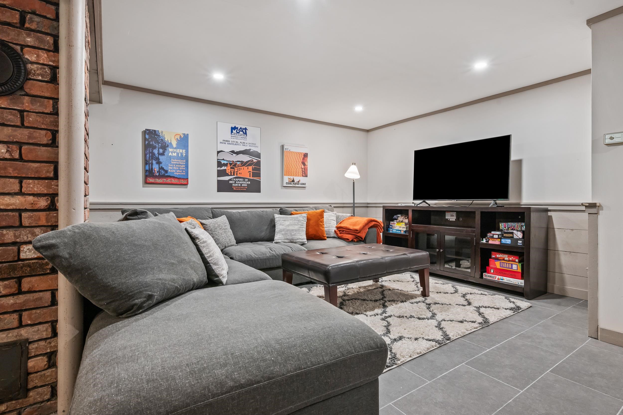 Living room with a gray sectional, orange accents, a television, and a brick fireplace wall.