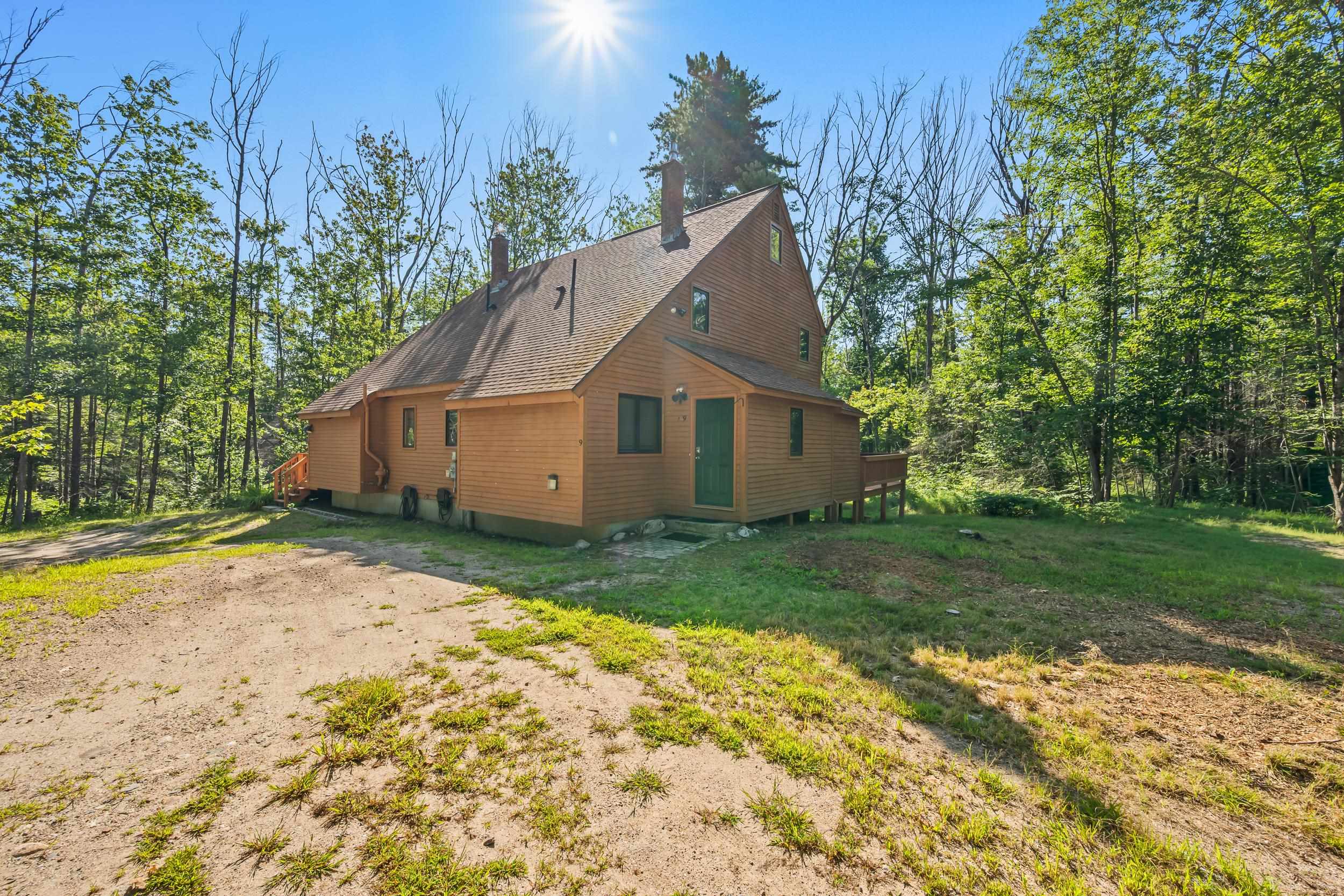 Wood-sided house with a steep gabled roof and green door among summer trees.
