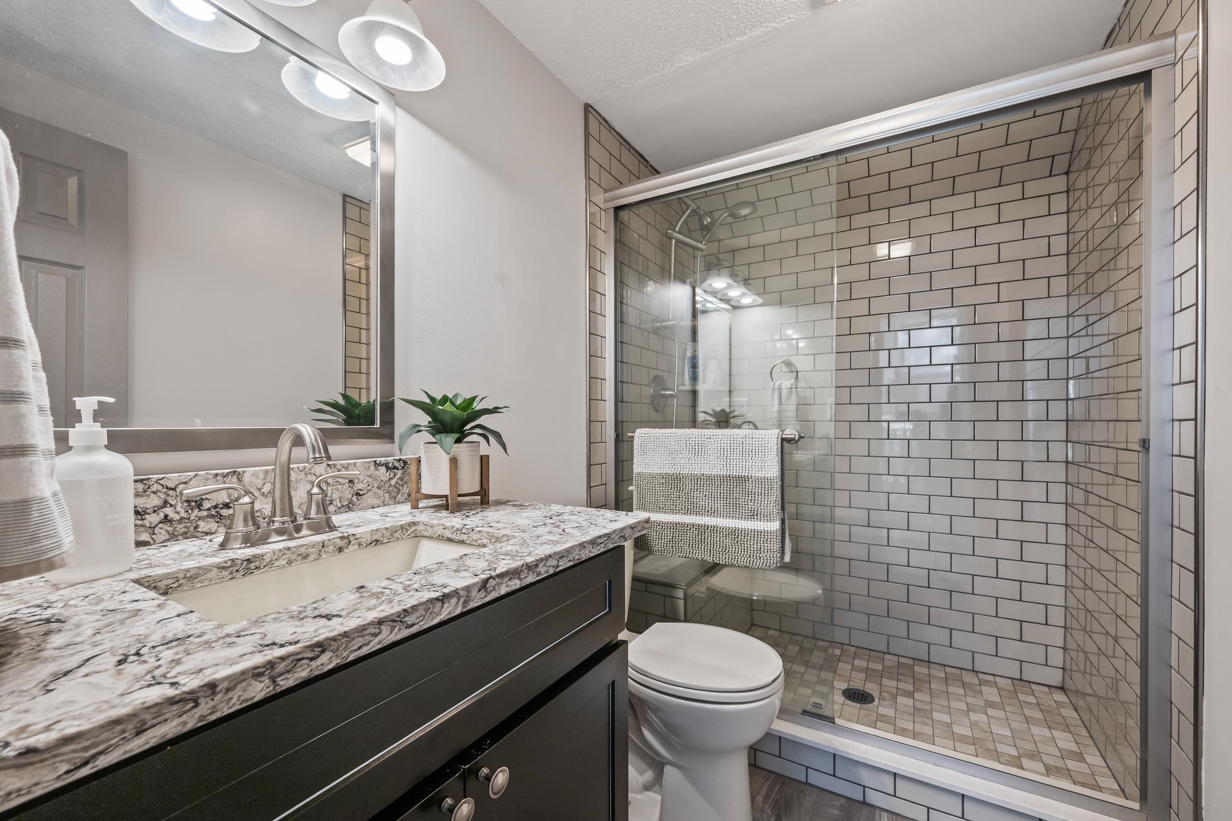 Bathroom with a marble vanity and a glass-enclosed white subway-tile shower.