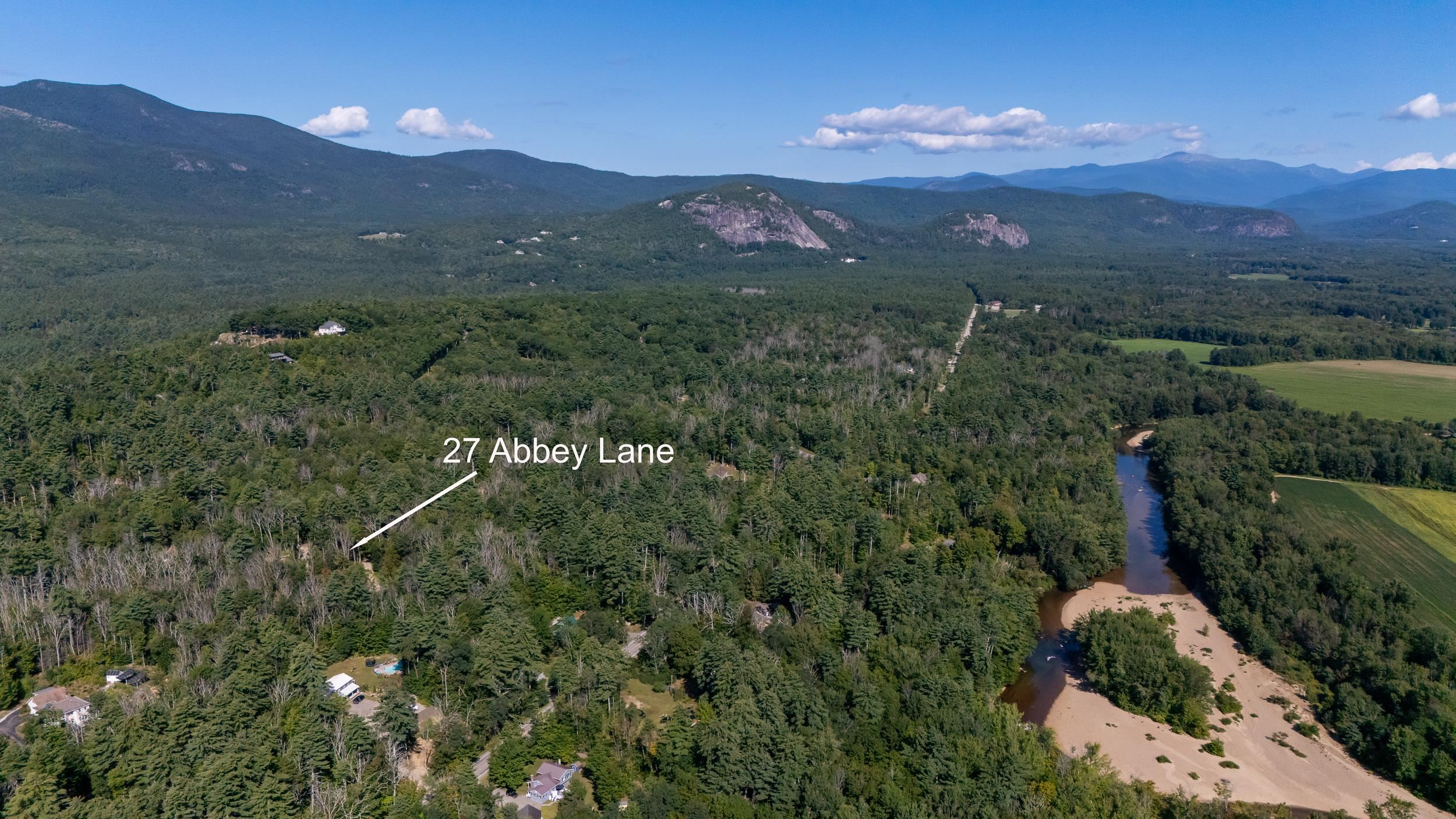 Aerial view of 27 Abbey Lane amid forest, with a river and mountain ranges nearby.