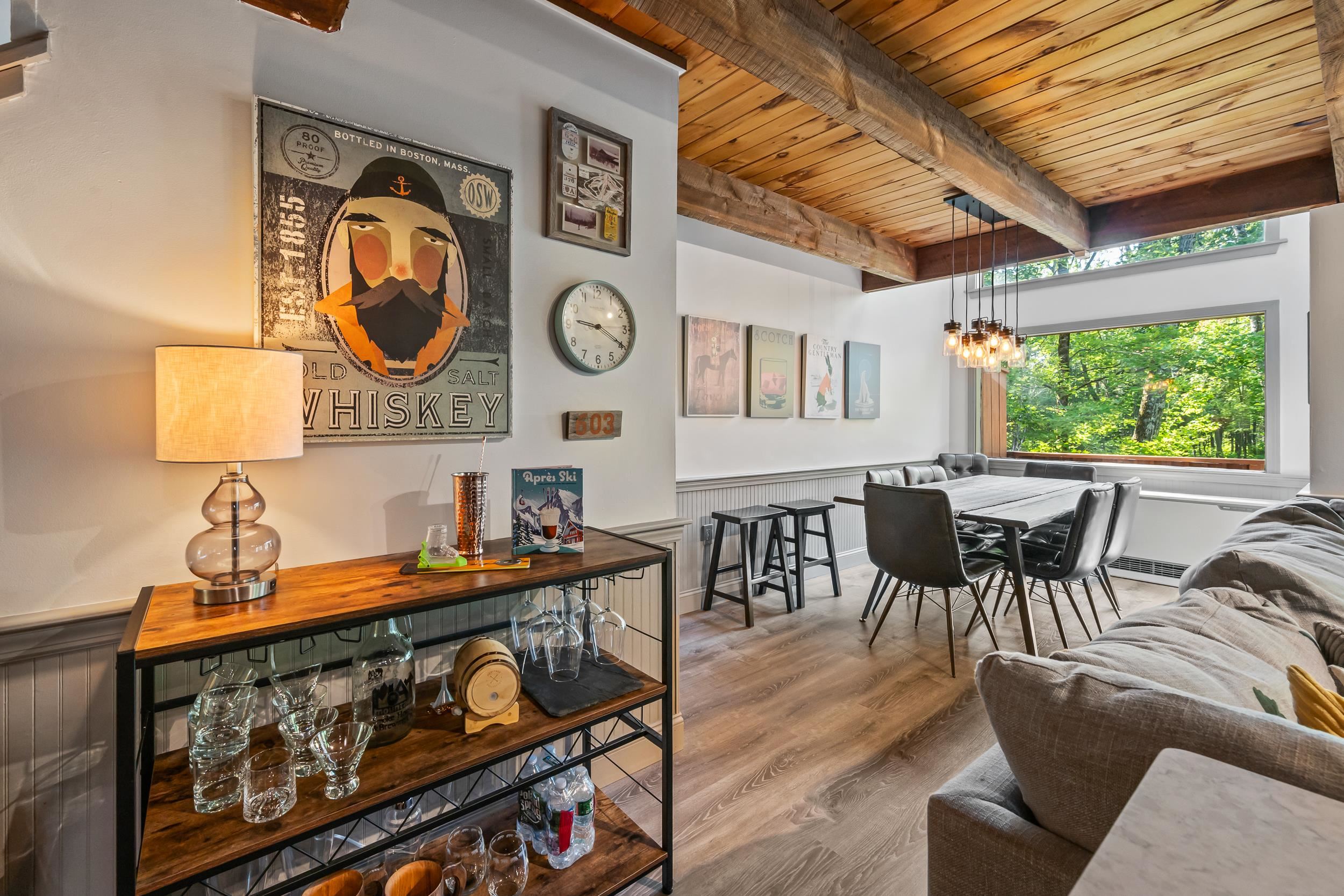 Open-plan living and dining area with exposed wood beams and a large window overlooking trees.