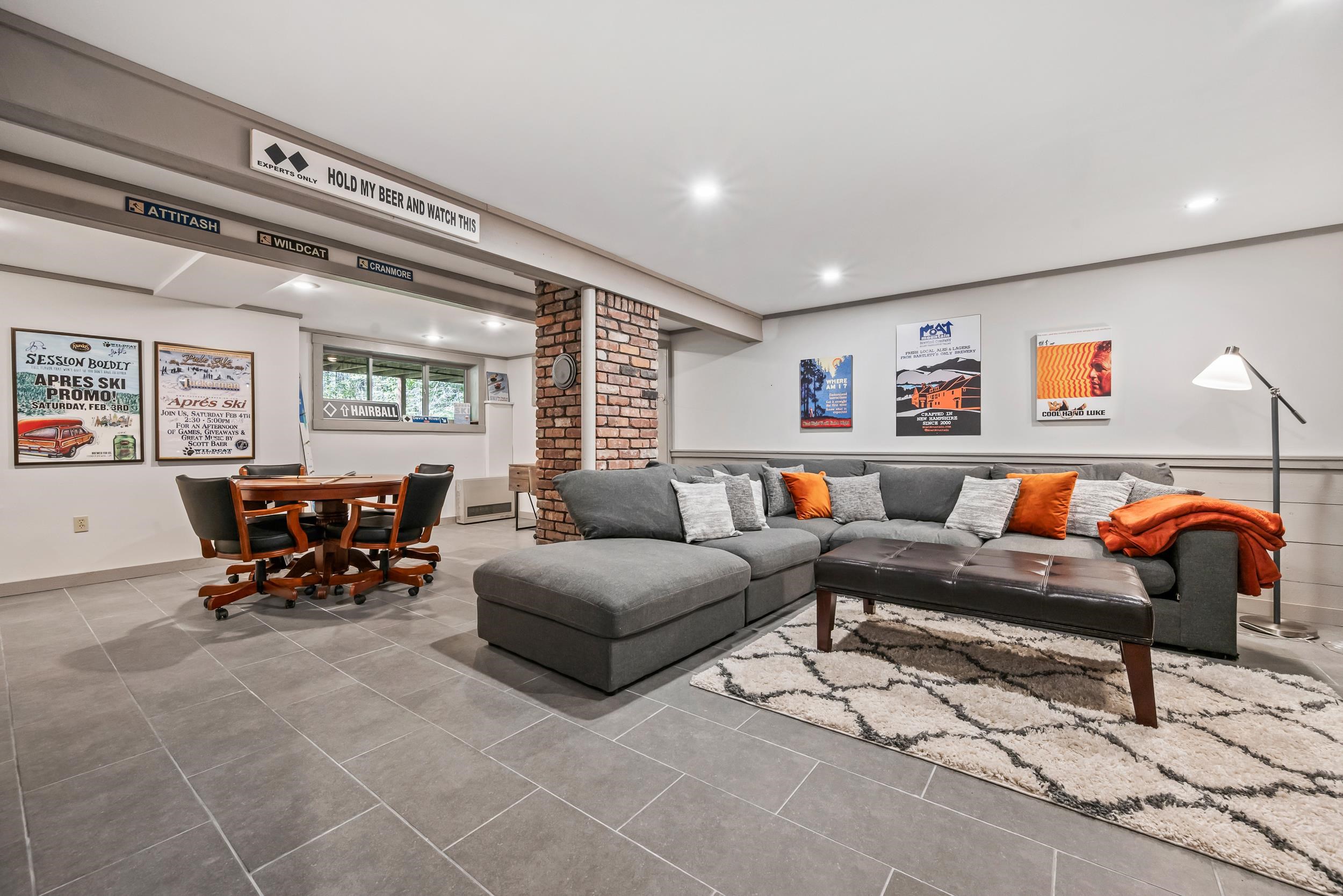 Furnished living room with a gray sectional, orange pillows, brick column, and adjoining dining area.