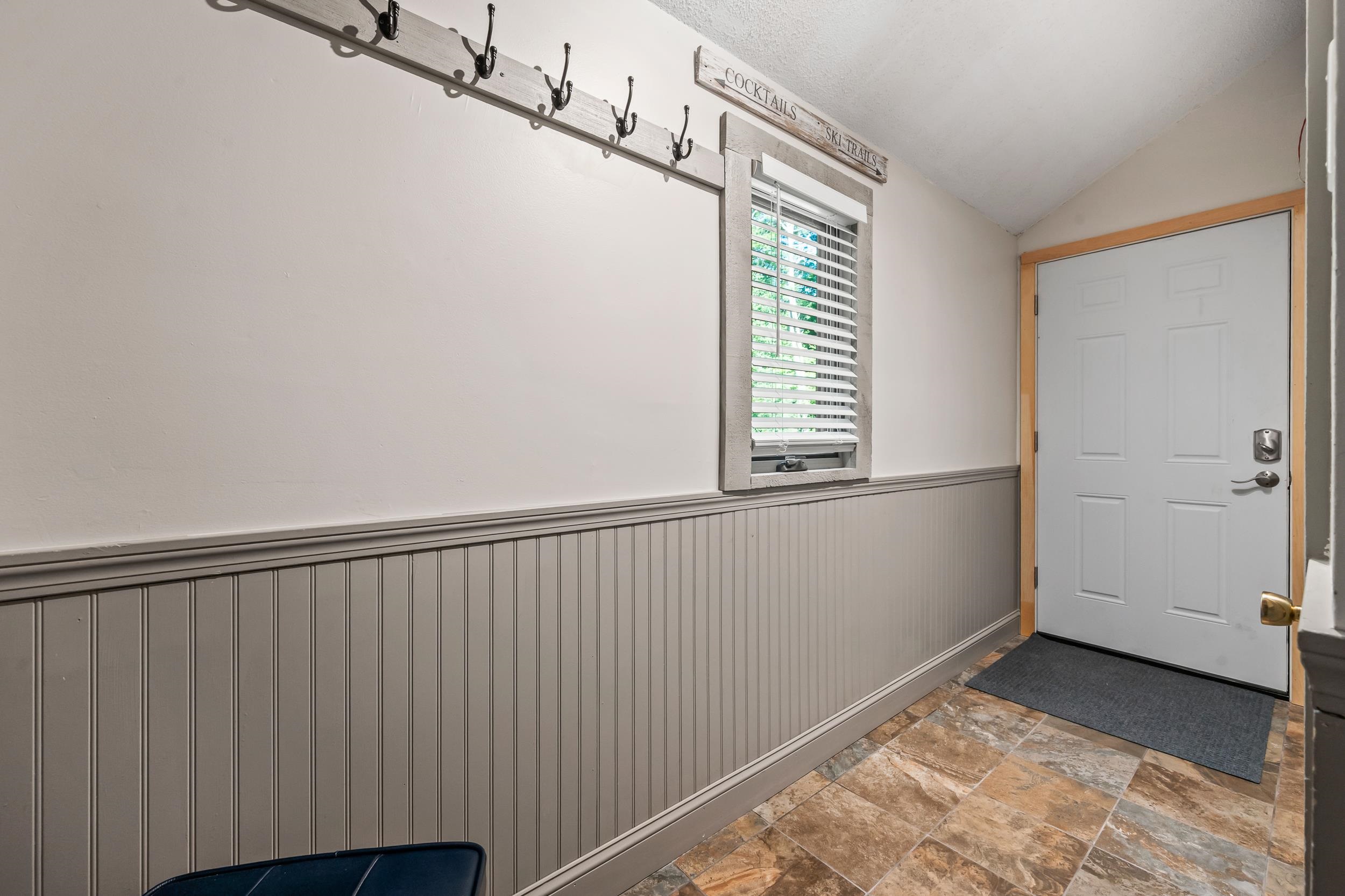 Entry hallway with coat hooks, gray beadboard wainscoting, patterned tile floor, and a white door.
