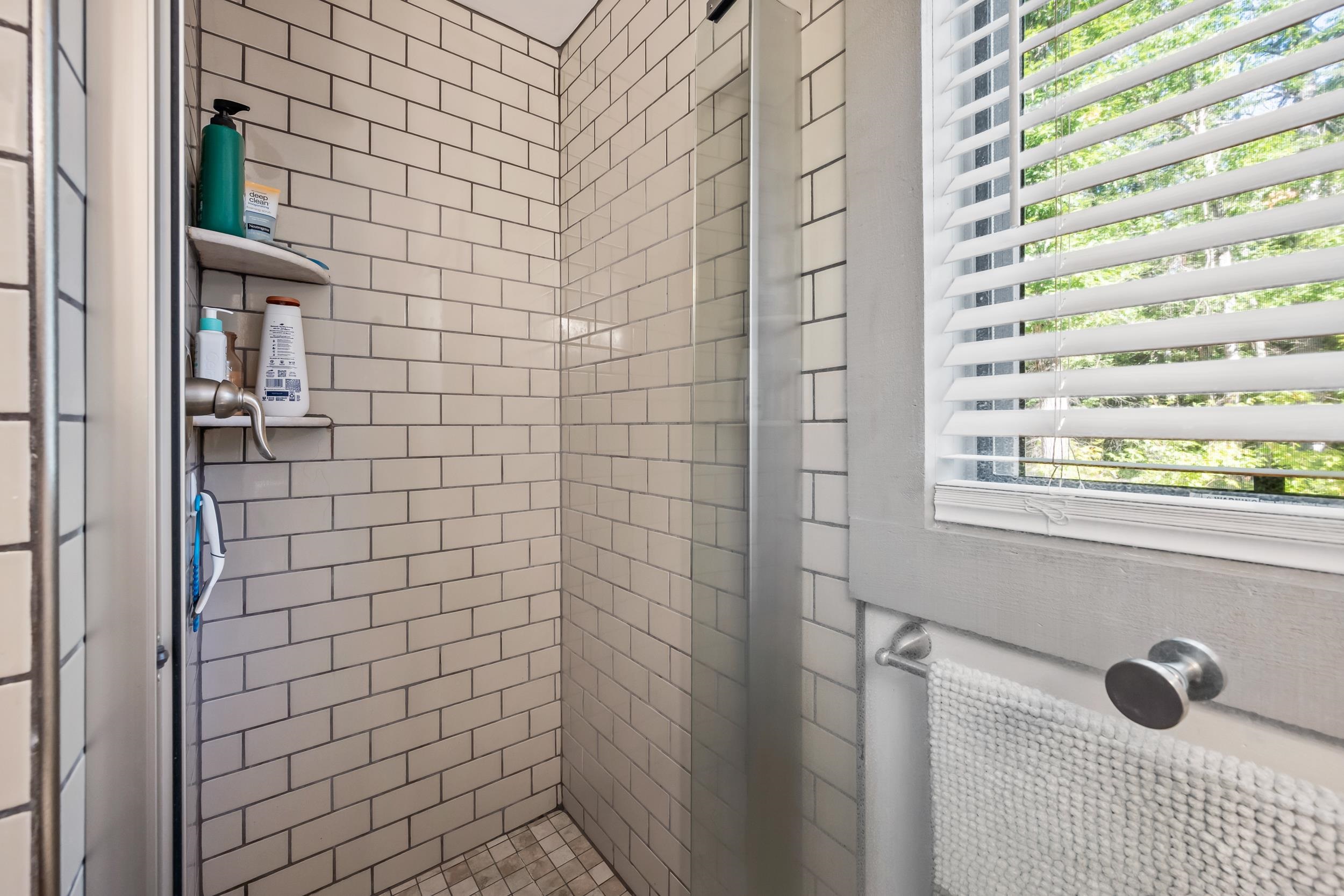 Tiled walk-in shower with glass enclosure, built-in shelves, and a shuttered window.