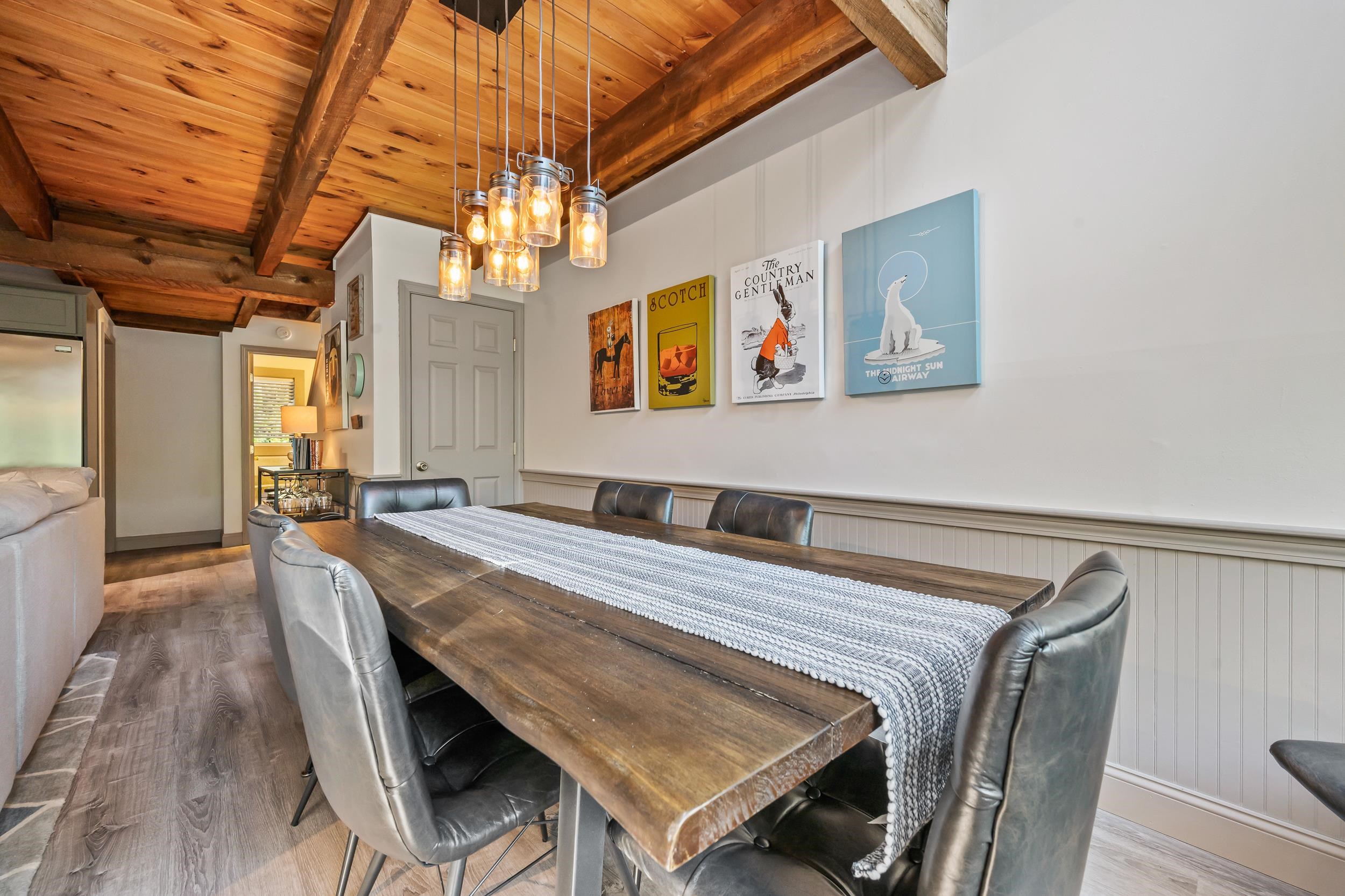 Dining room with a rustic table, leather chairs, exposed timber ceiling, and glass pendant lights.