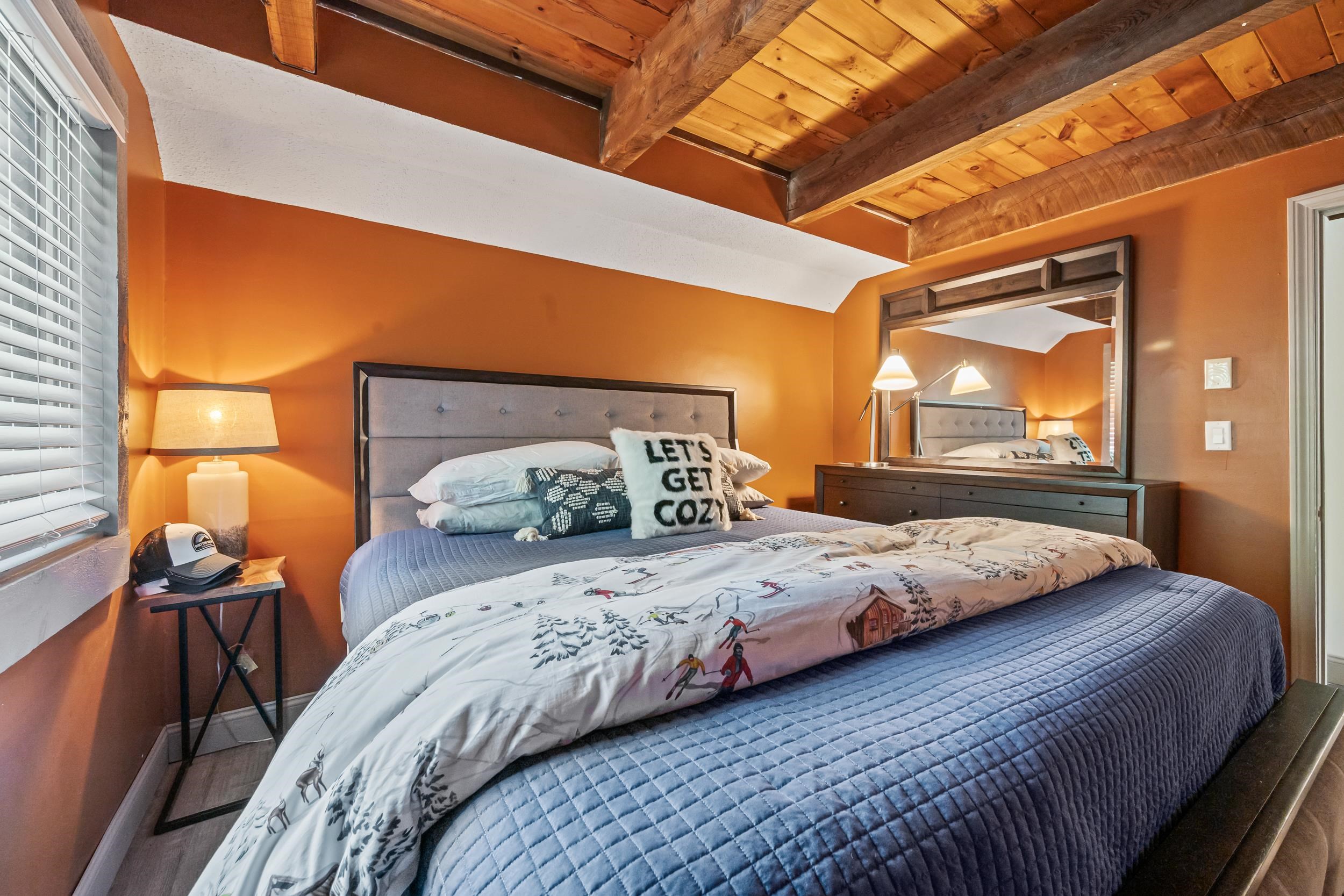 Bedroom with orange walls, exposed timber ceiling beams, and a large bed dressed in blue and ski-print bedding.