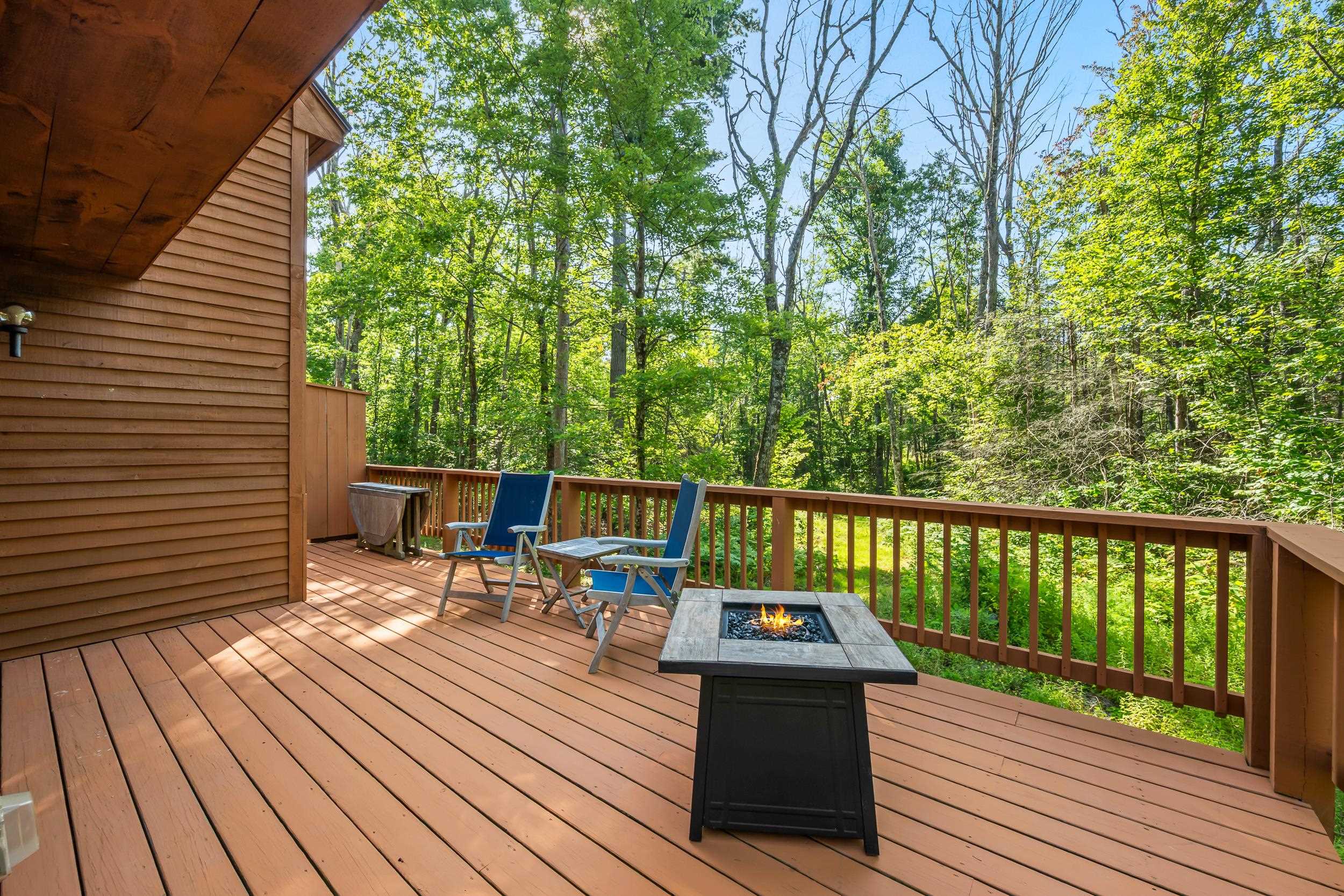 Wooden deck with blue chairs and a fire table overlooking the woods.