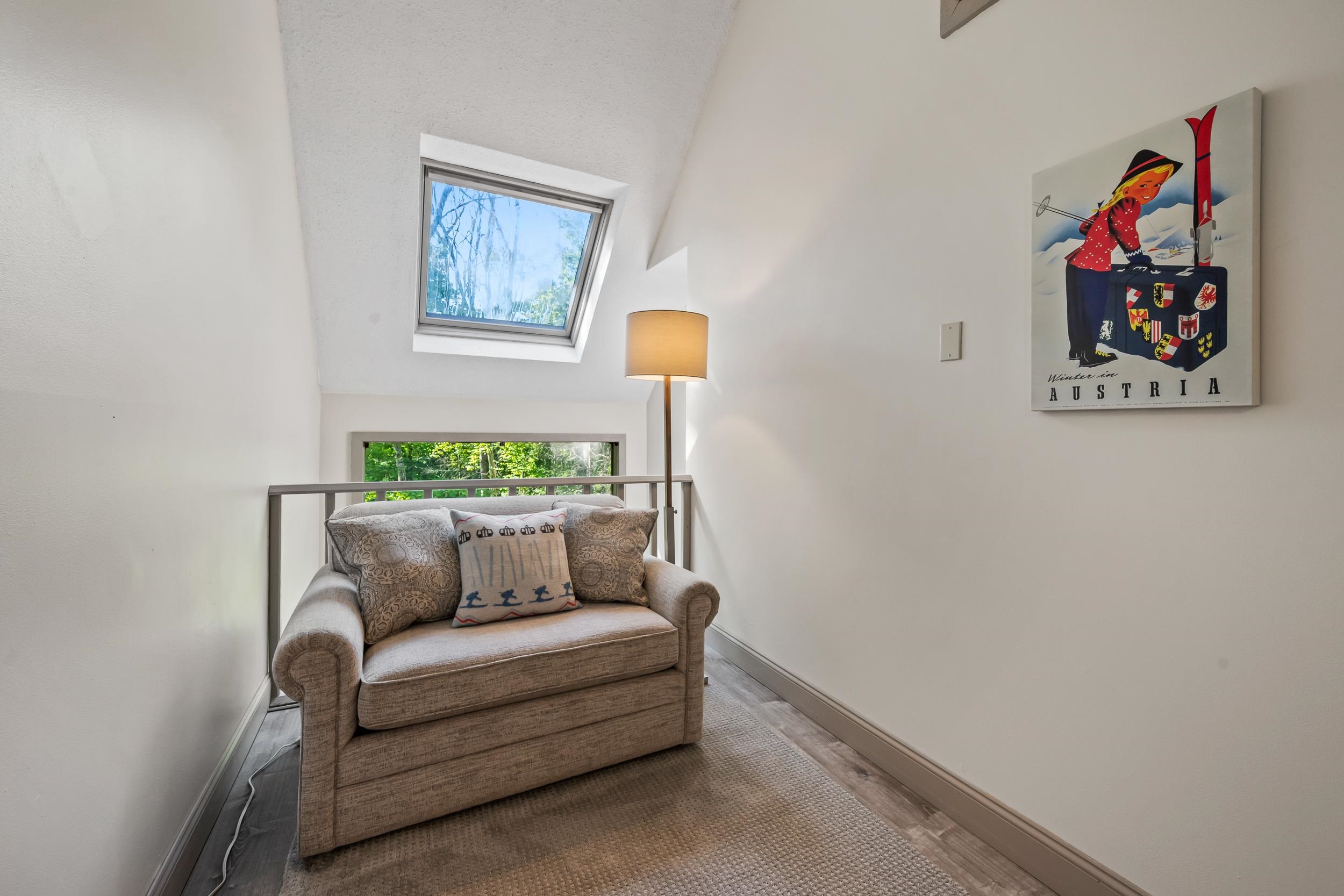 Furnished upstairs sitting nook with a beige armchair, skylight, and Austria ski poster.