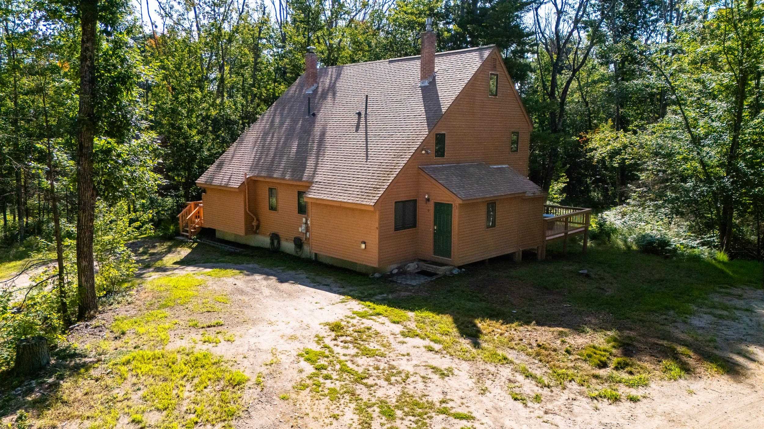 Brown gabled home with a green front door and deck, surrounded by trees.
