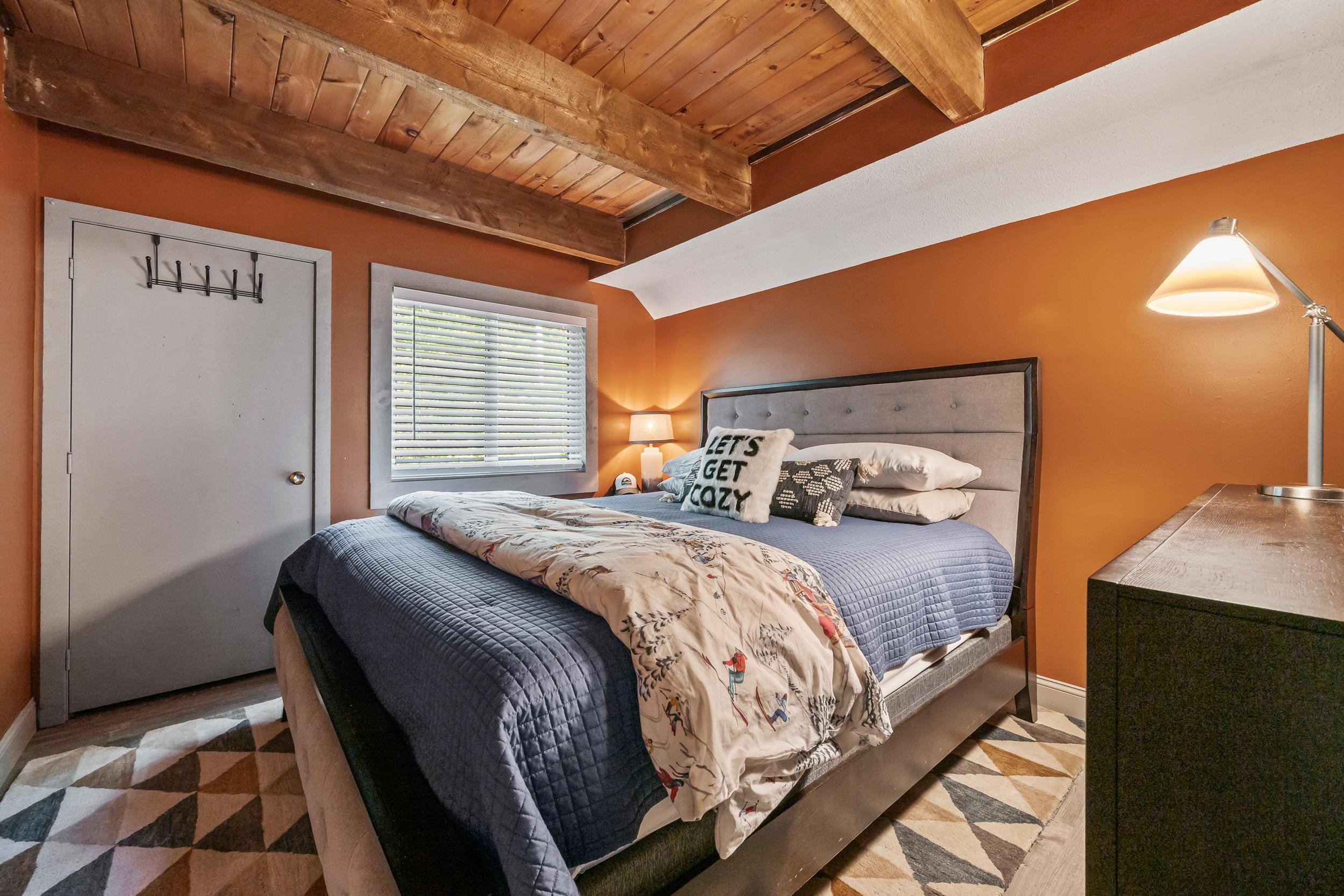Bedroom with exposed wooden ceiling beams, terracotta walls, and a bed with blue and patterned bedding.