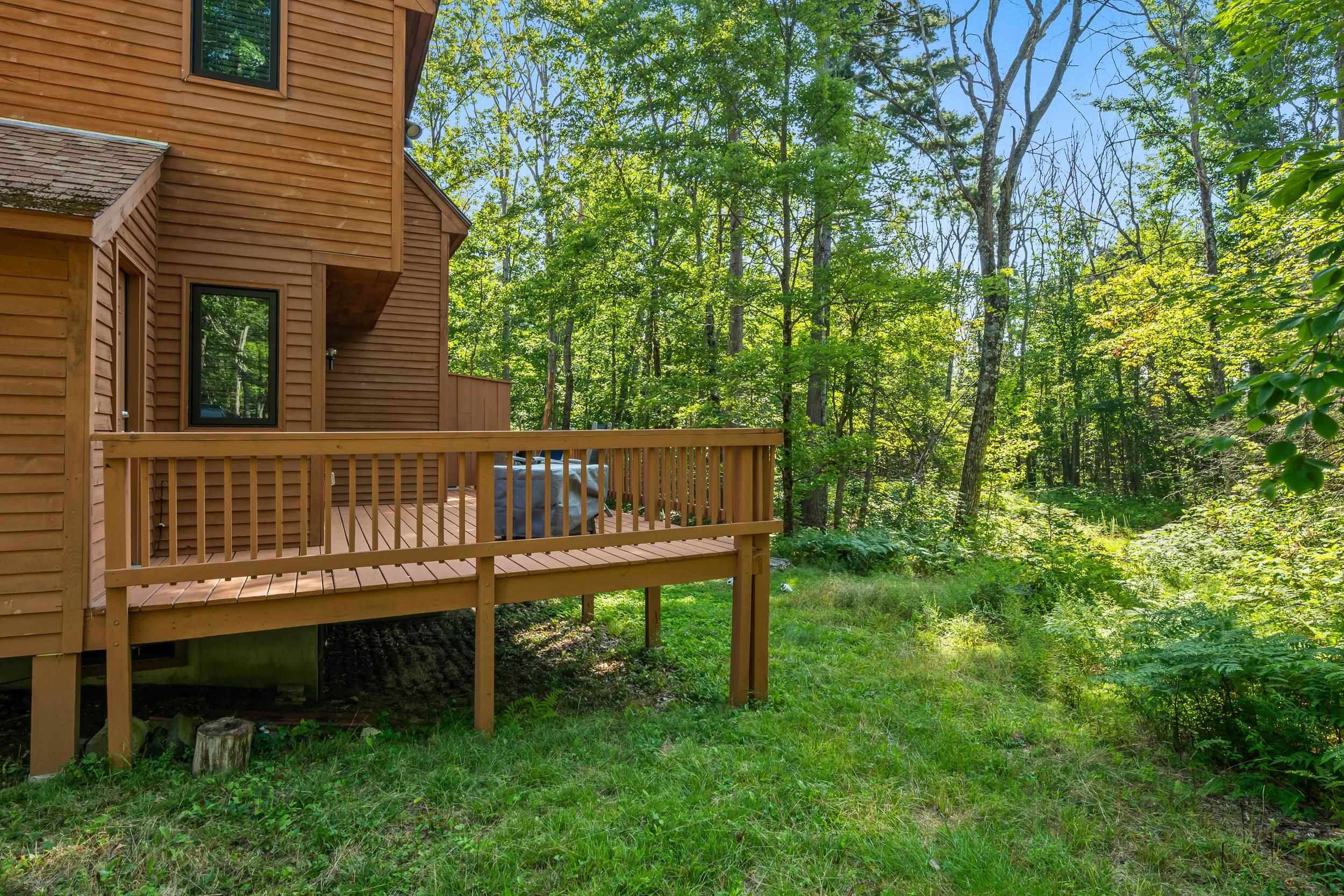 Raised deck beside a brown-sided home, with a covered hot tub and wooded surroundings.