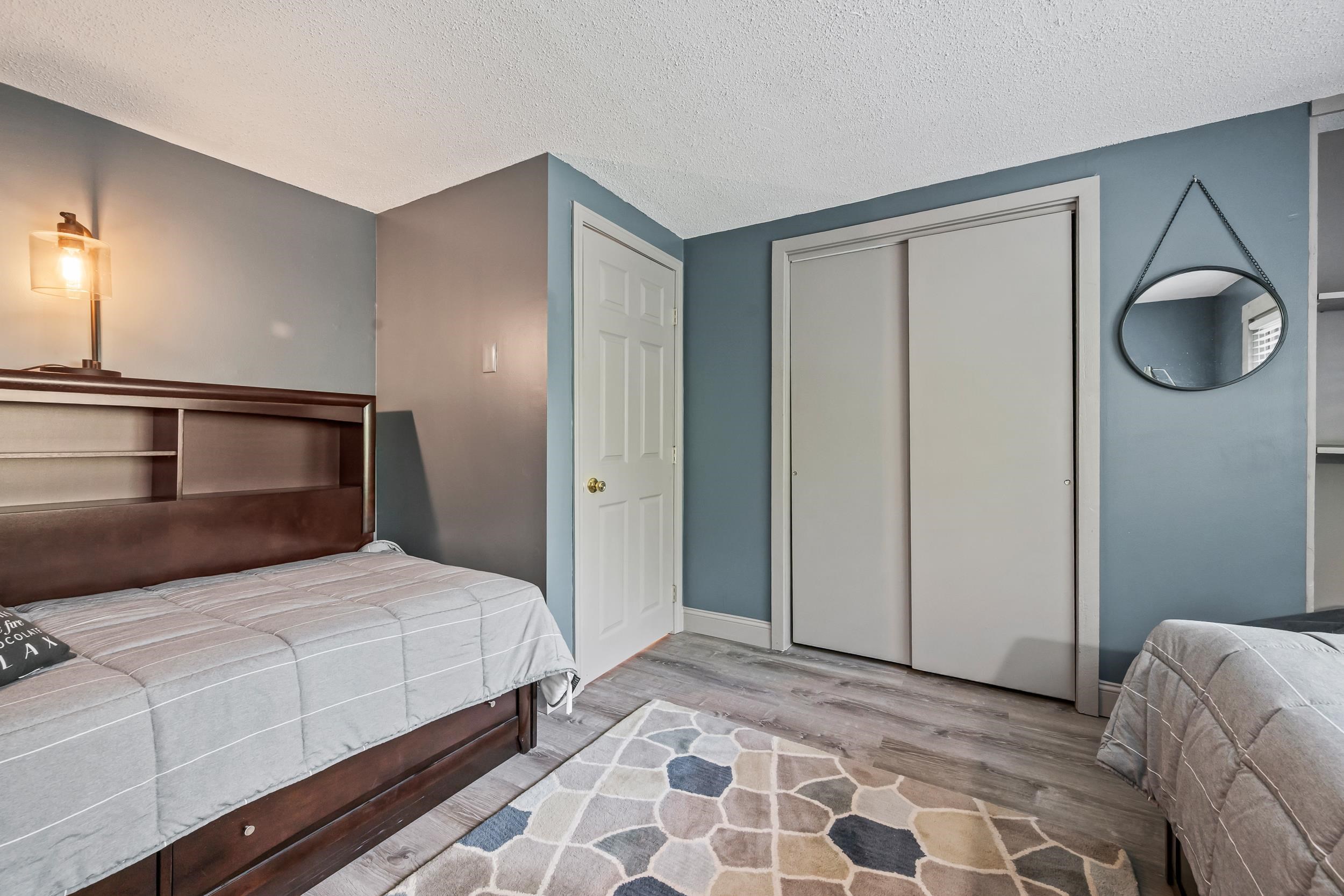 Bedroom with a gray-covered bed, built-in headboard shelves, sliding closet doors, and a geometric rug.