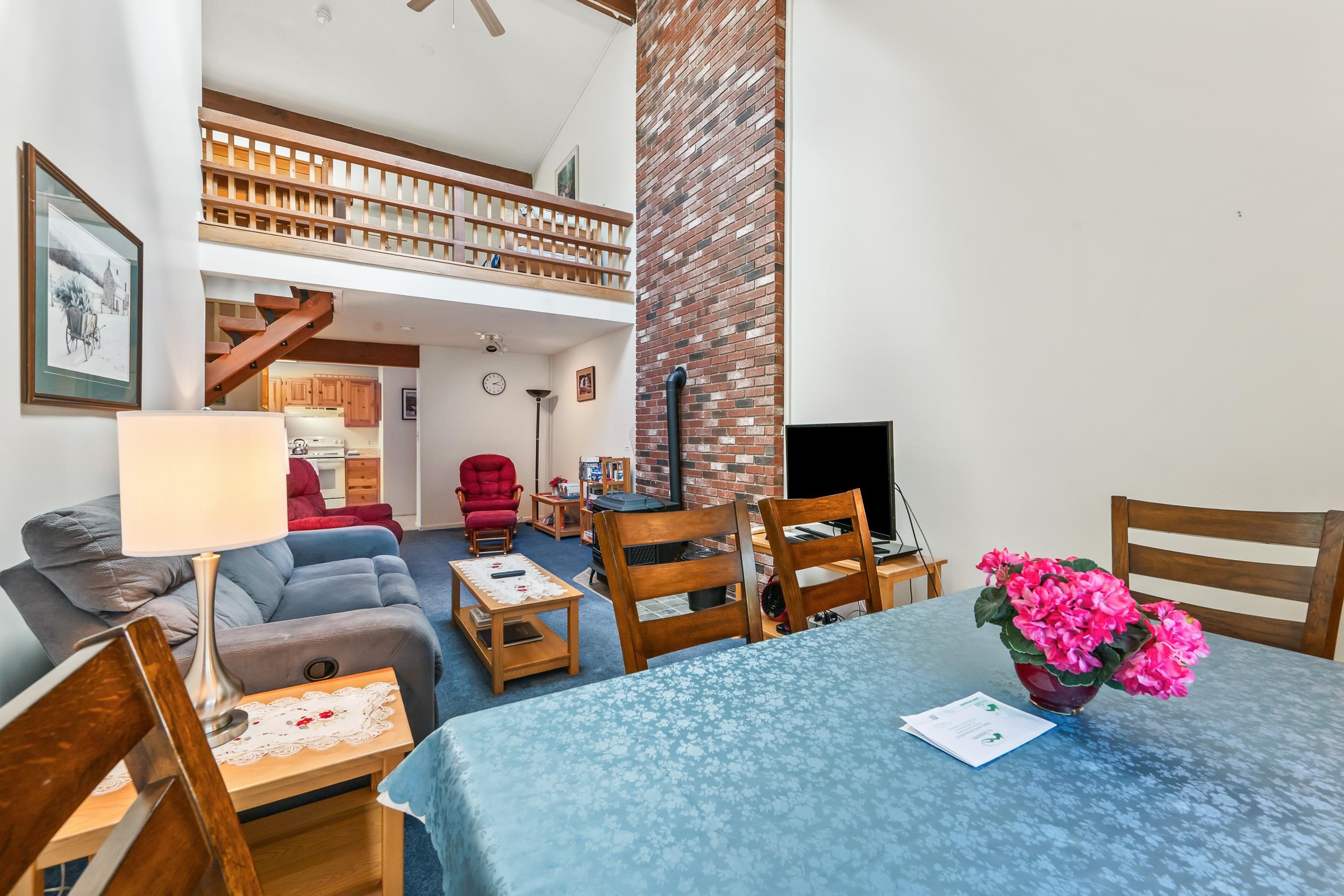 Open-plan living and dining room with a brick chimney, loft railing, and pink flowers on the table.