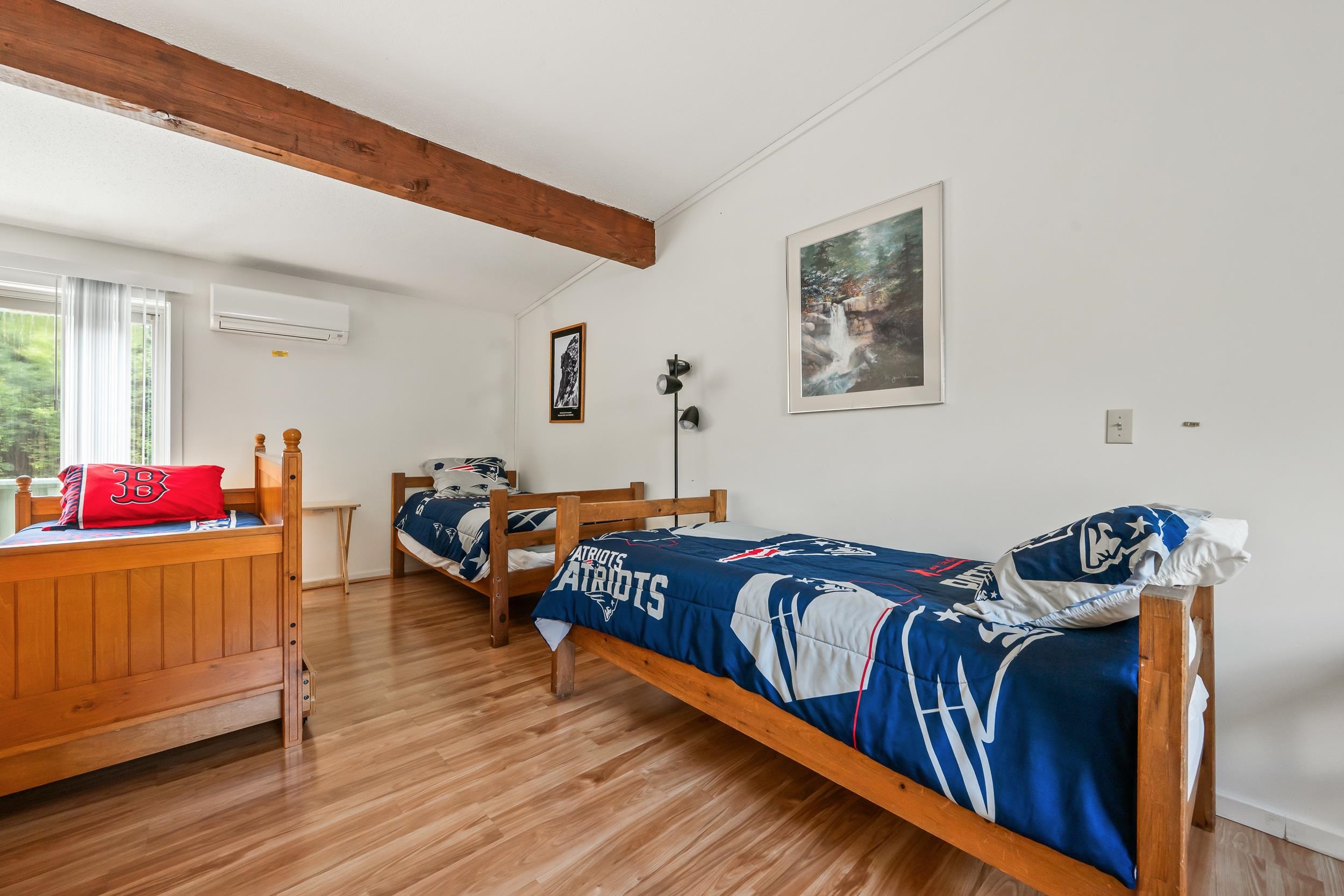 Bedroom with three wooden single beds, Patriots bedding, a Red Sox pillow, and an exposed ceiling beam.