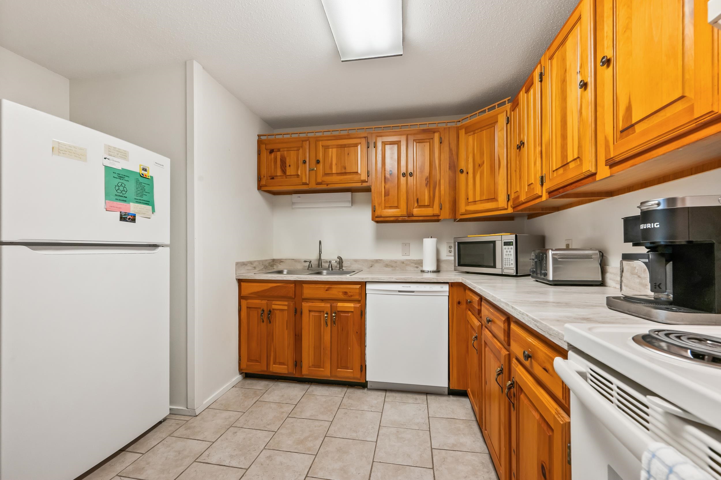 Kitchen with honey-colored wood cabinets, light countertops, and white appliances.