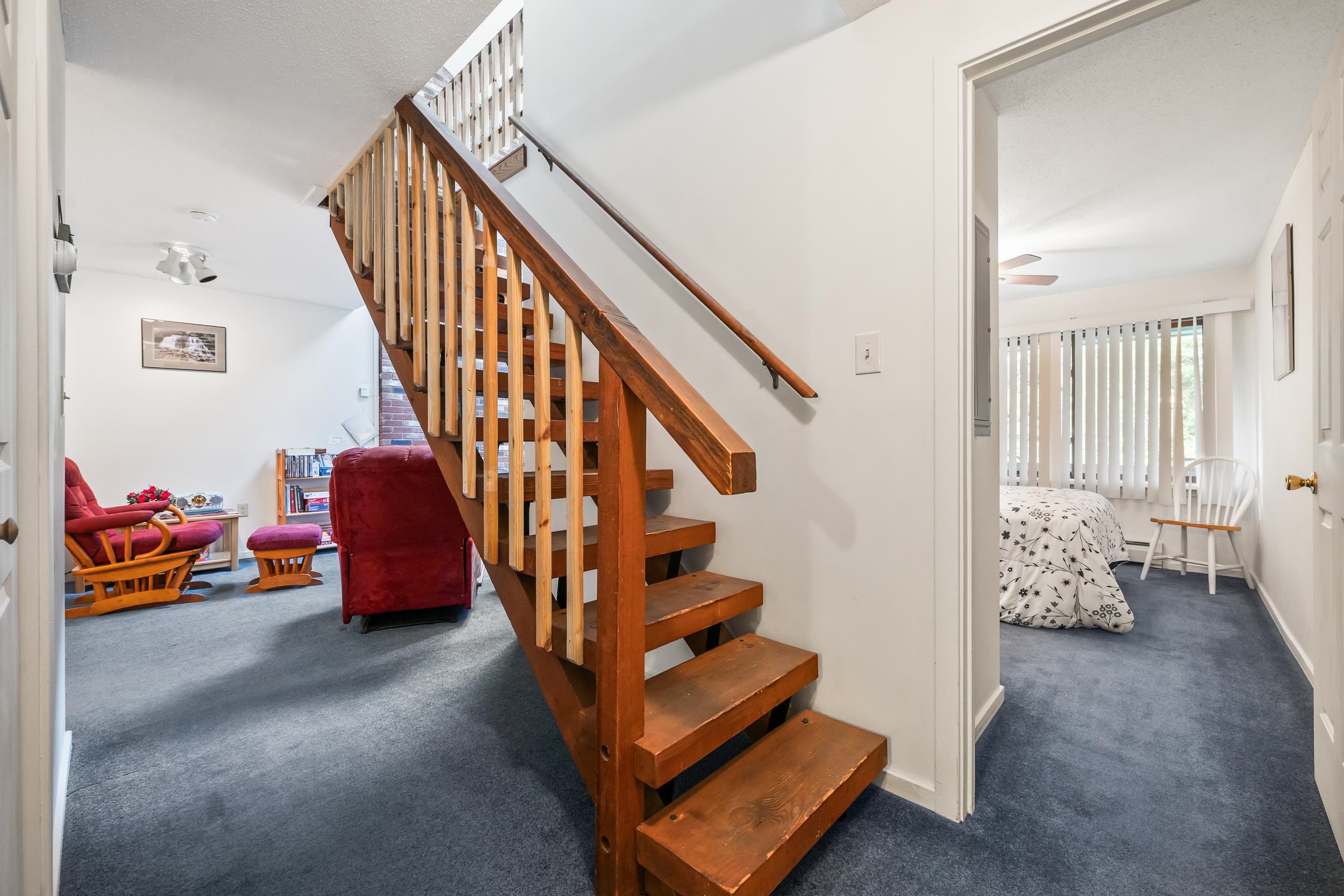 Wooden staircase between a red-furnished living room and a bedroom.