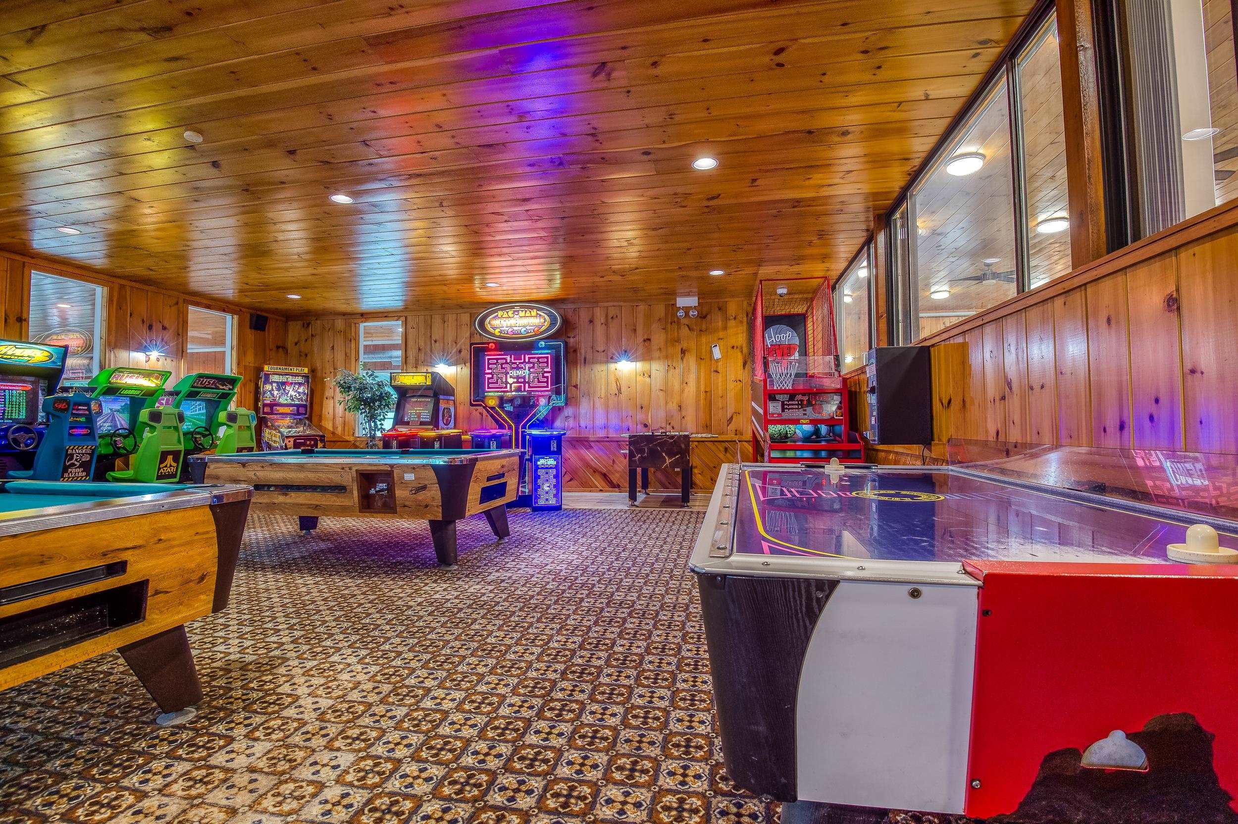 Wood-paneled game room with arcade games, pool tables, and an air hockey table.
