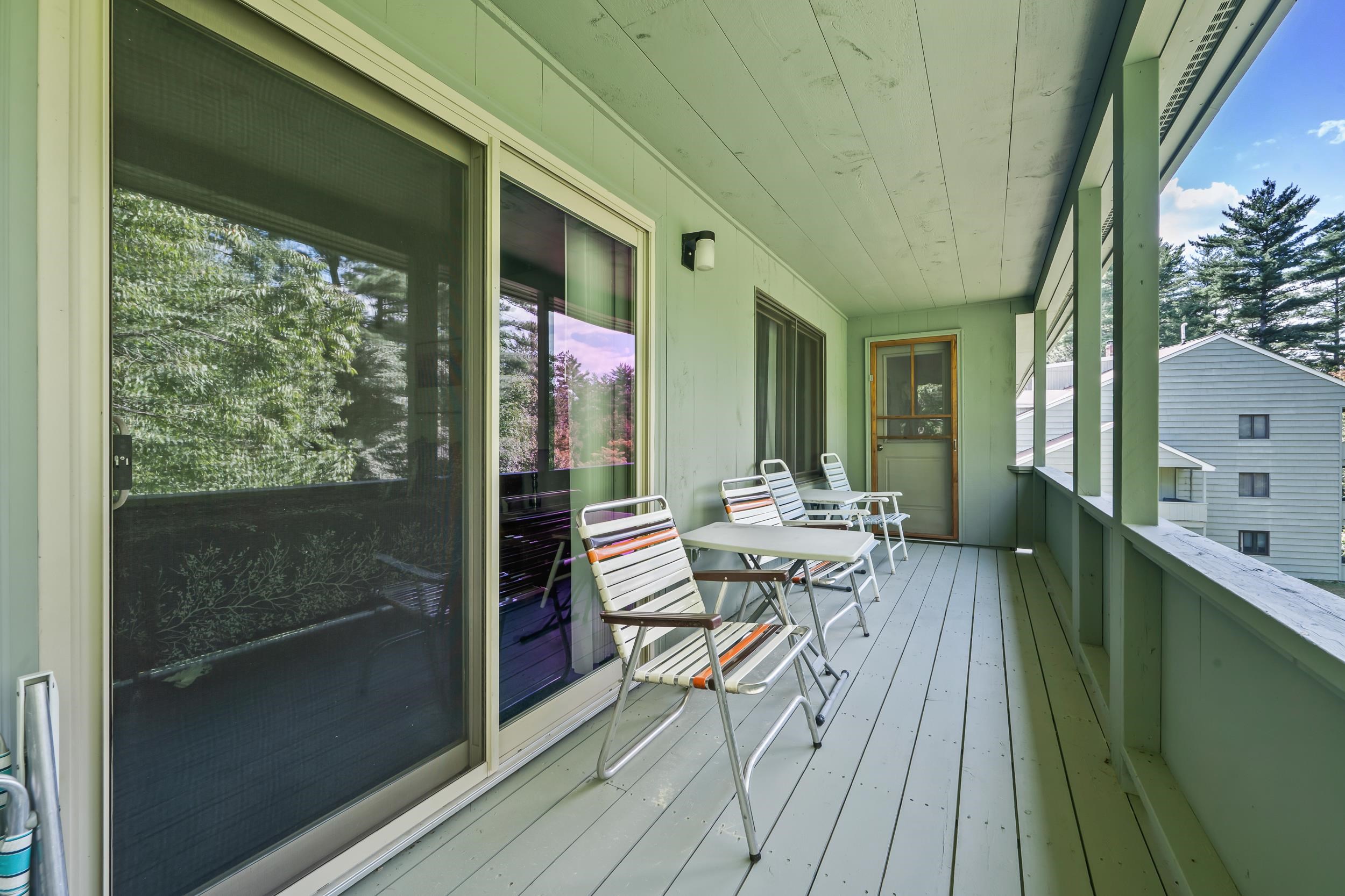 Covered balcony with white patio furniture, sliding glass doors, and trees visible beyond the railing.