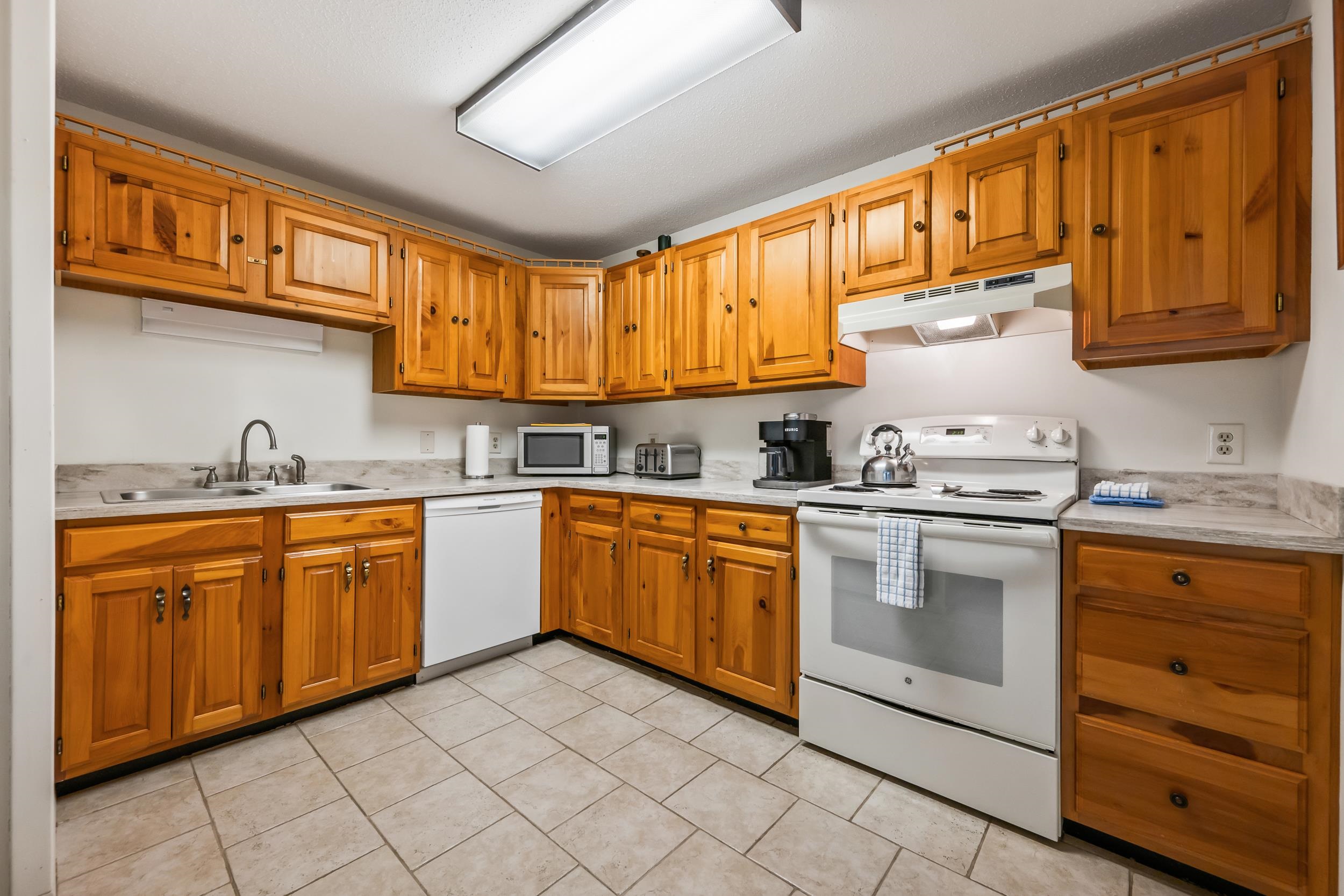 Kitchen with honey-colored wood cabinets, tiled floor, and white appliances.