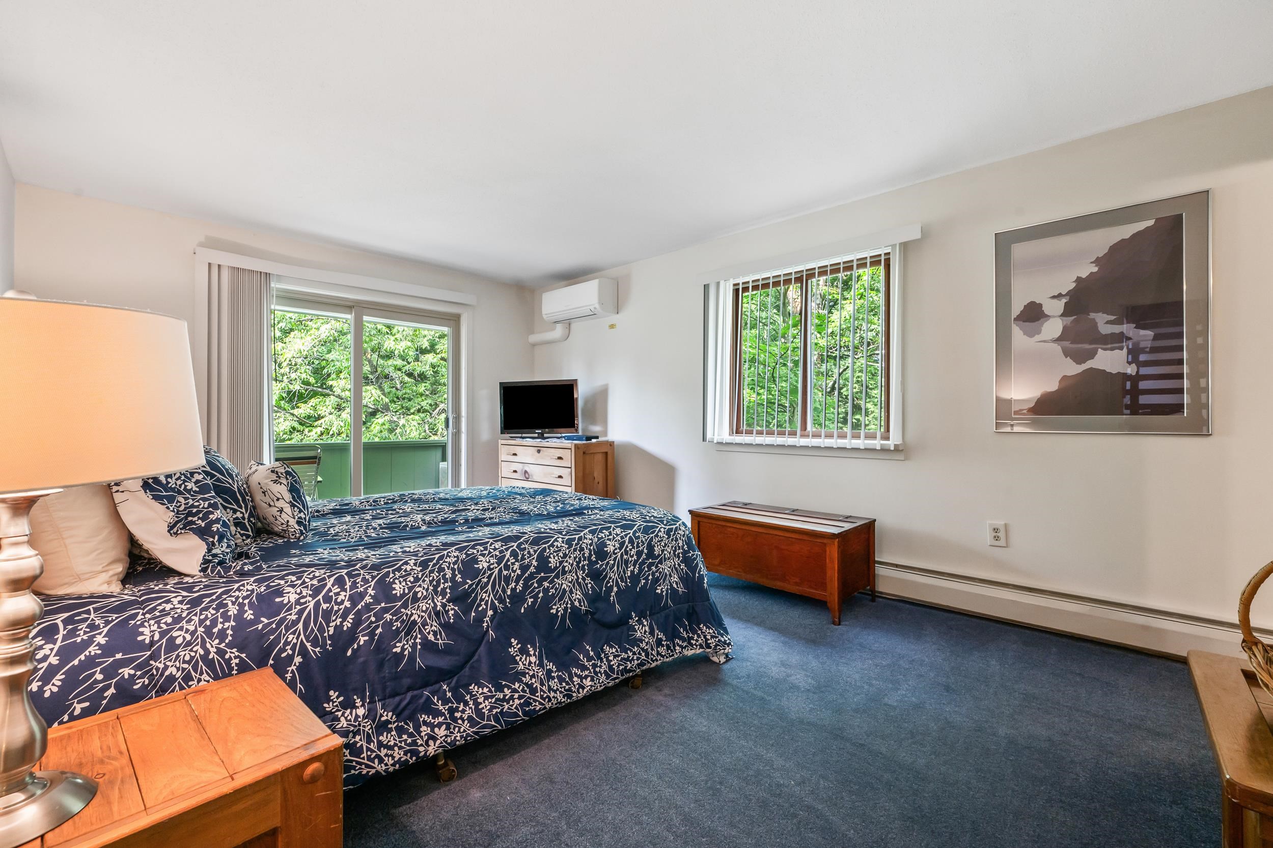 Furnished bedroom with navy floral bedding, wooden furniture, and sliding doors opening to leafy greenery.