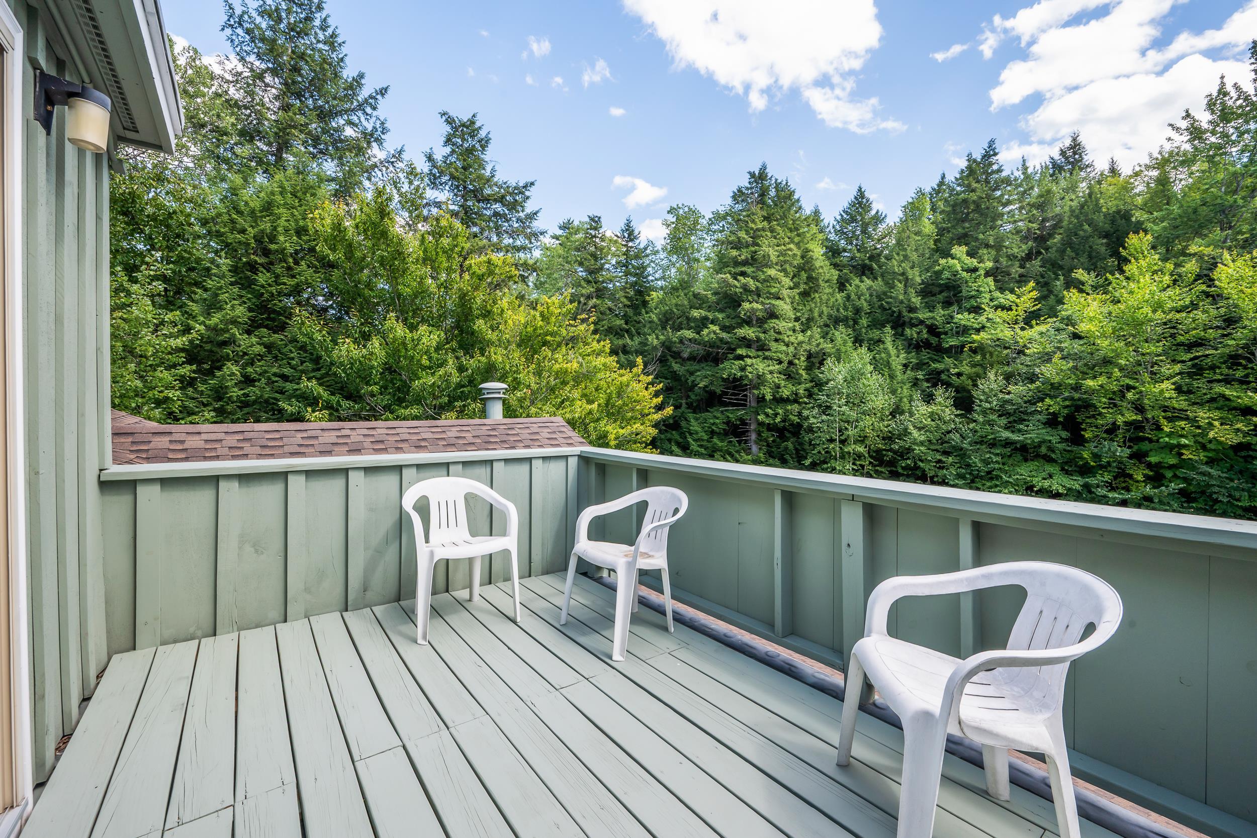 Balcony with three white chairs overlooking a dense green forest.