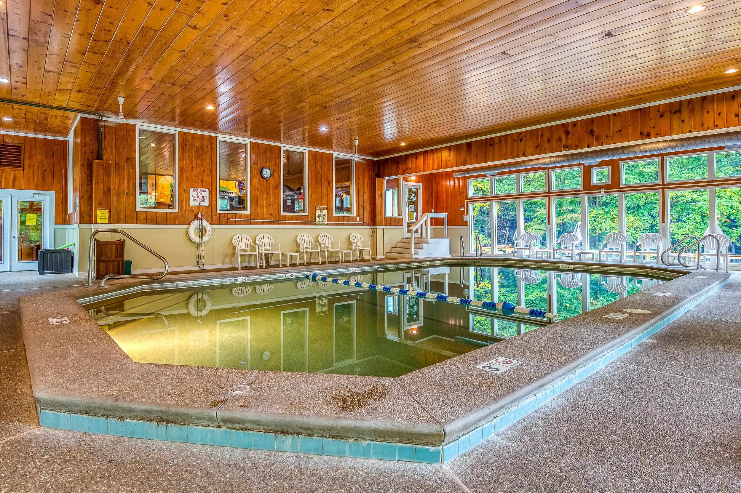 Indoor pool with wood-paneled walls, a lane divider, and large windows overlooking trees.