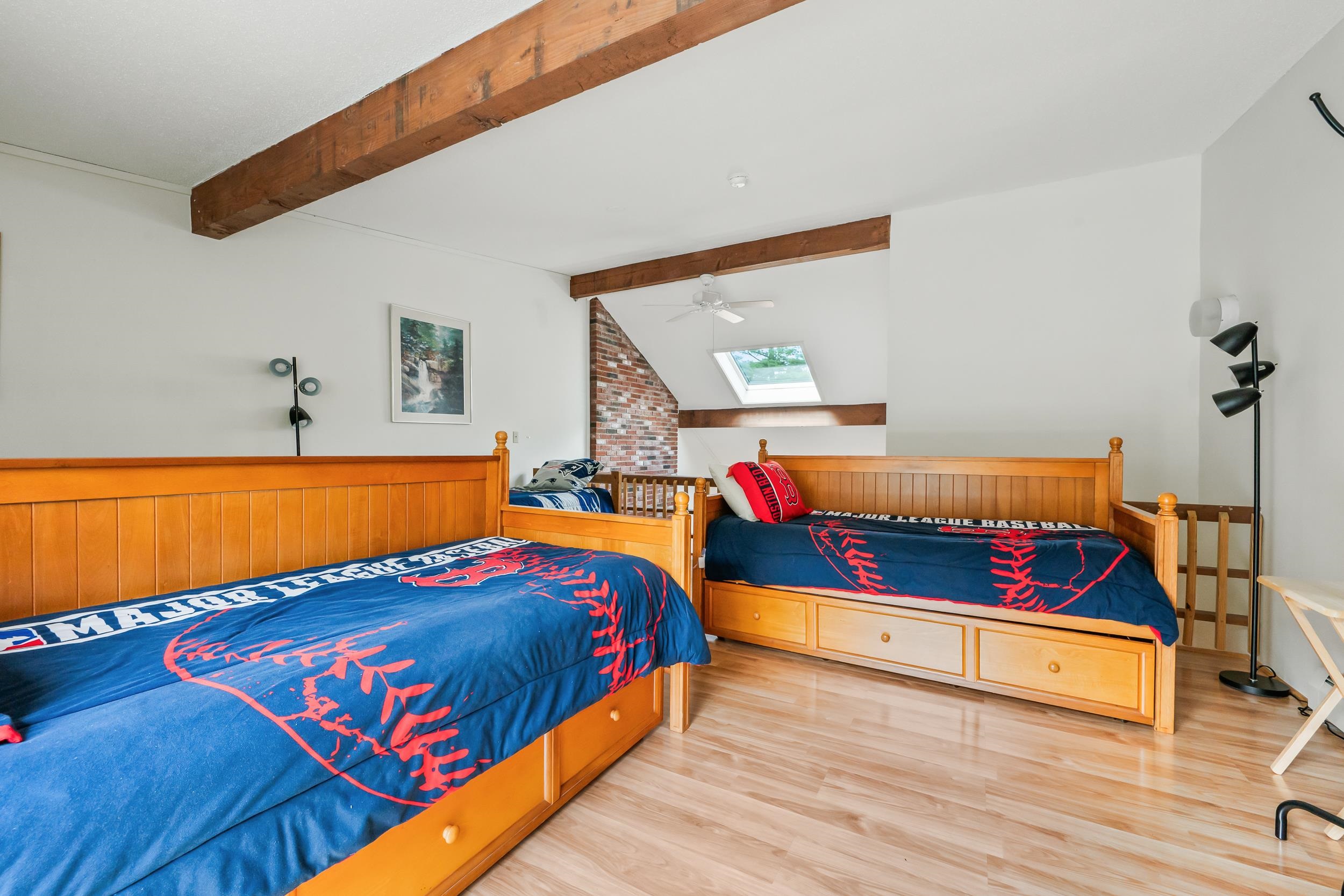 Bedroom with two wooden beds, baseball bedding, exposed beams, and a skylight.