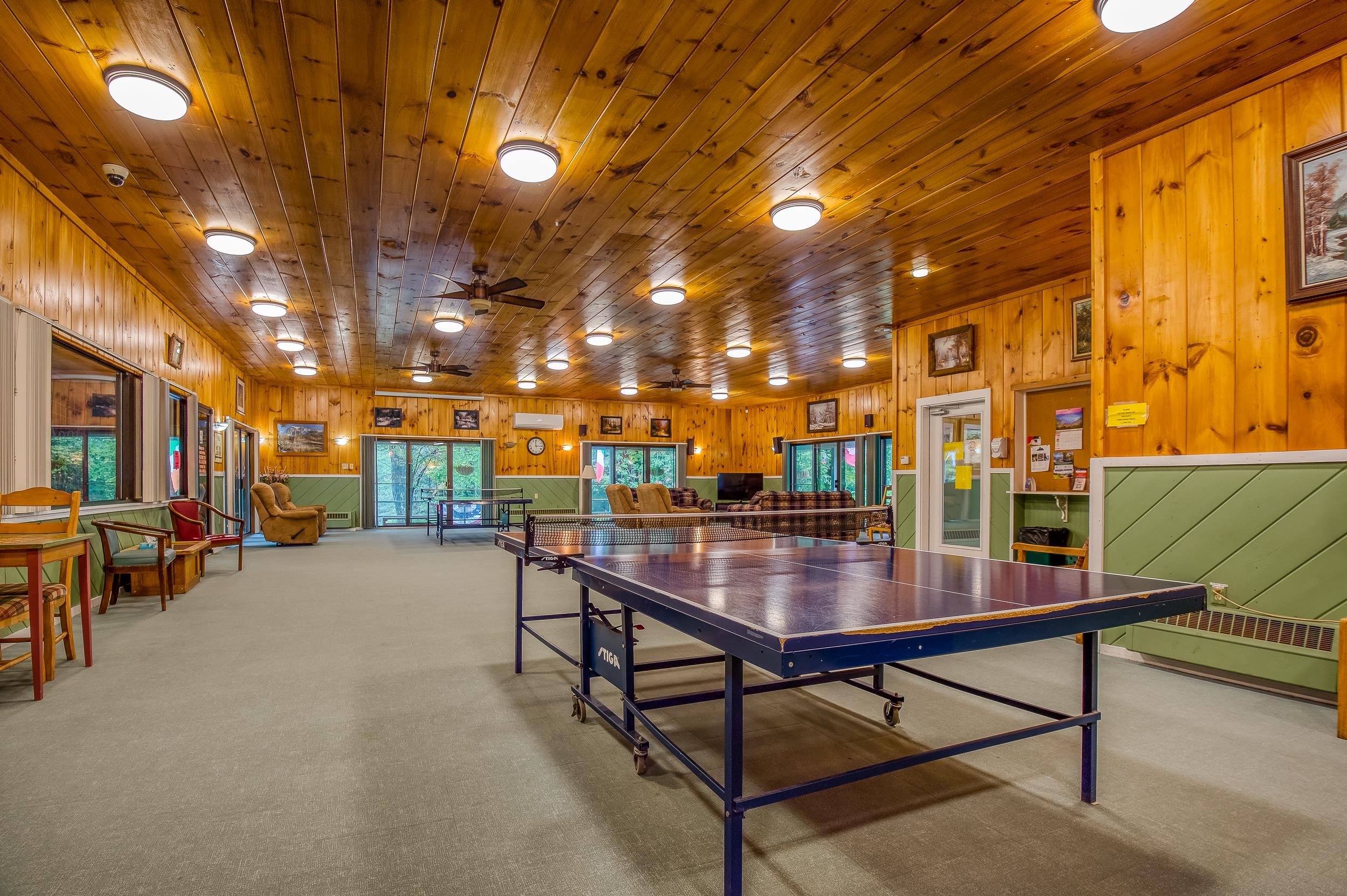 Recreation room with a large ping-pong table, wood paneling, green wainscoting, and lounge seating.