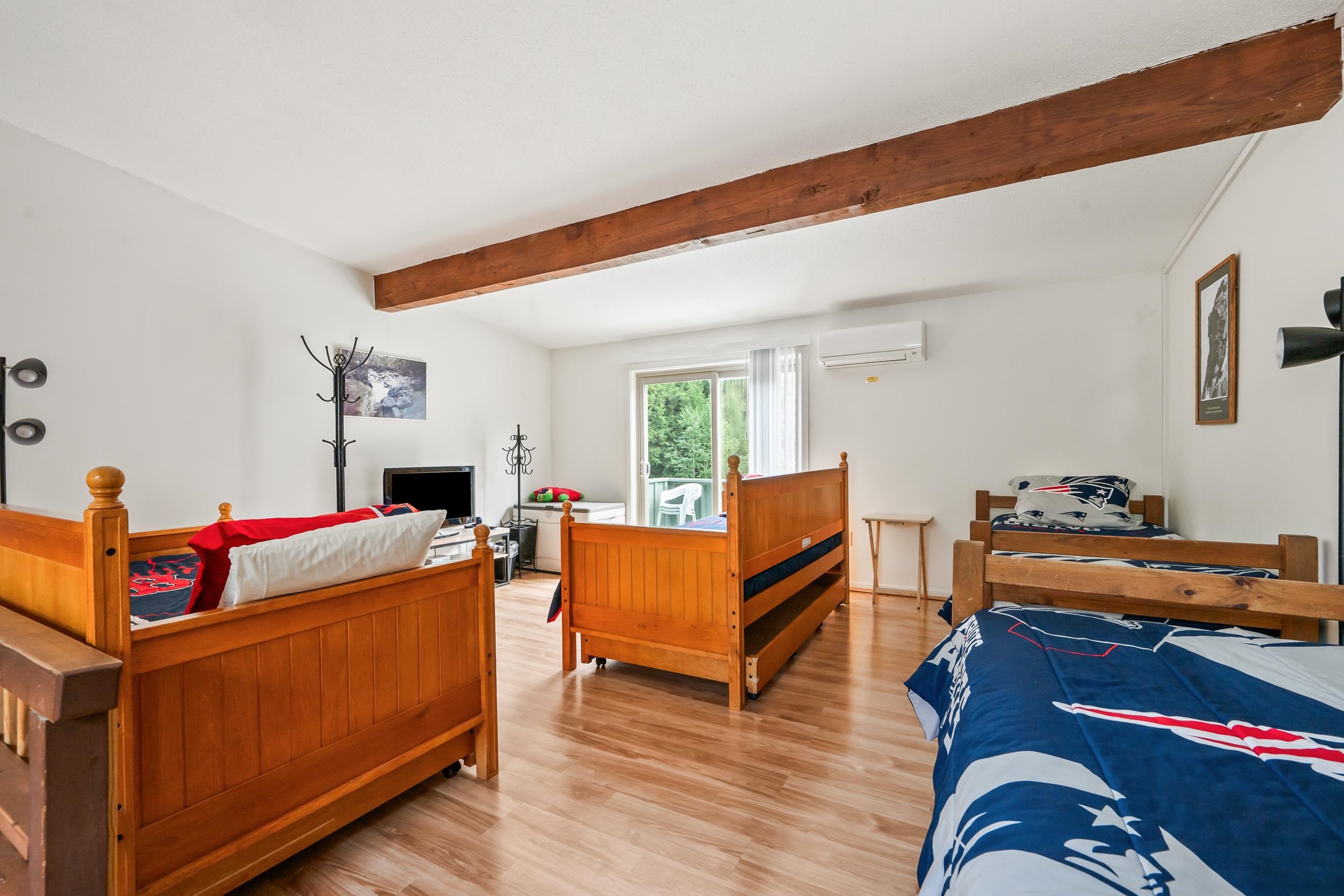 Bedroom with three wooden beds, Patriots bedding, an exposed ceiling beam, and a sliding glass door.