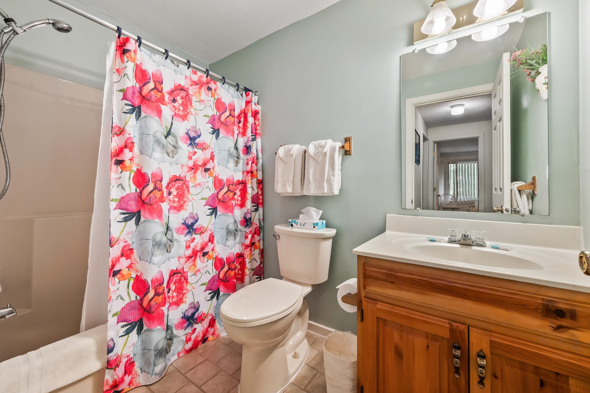 Bathroom with a vivid floral shower curtain, white toilet, and wooden vanity.