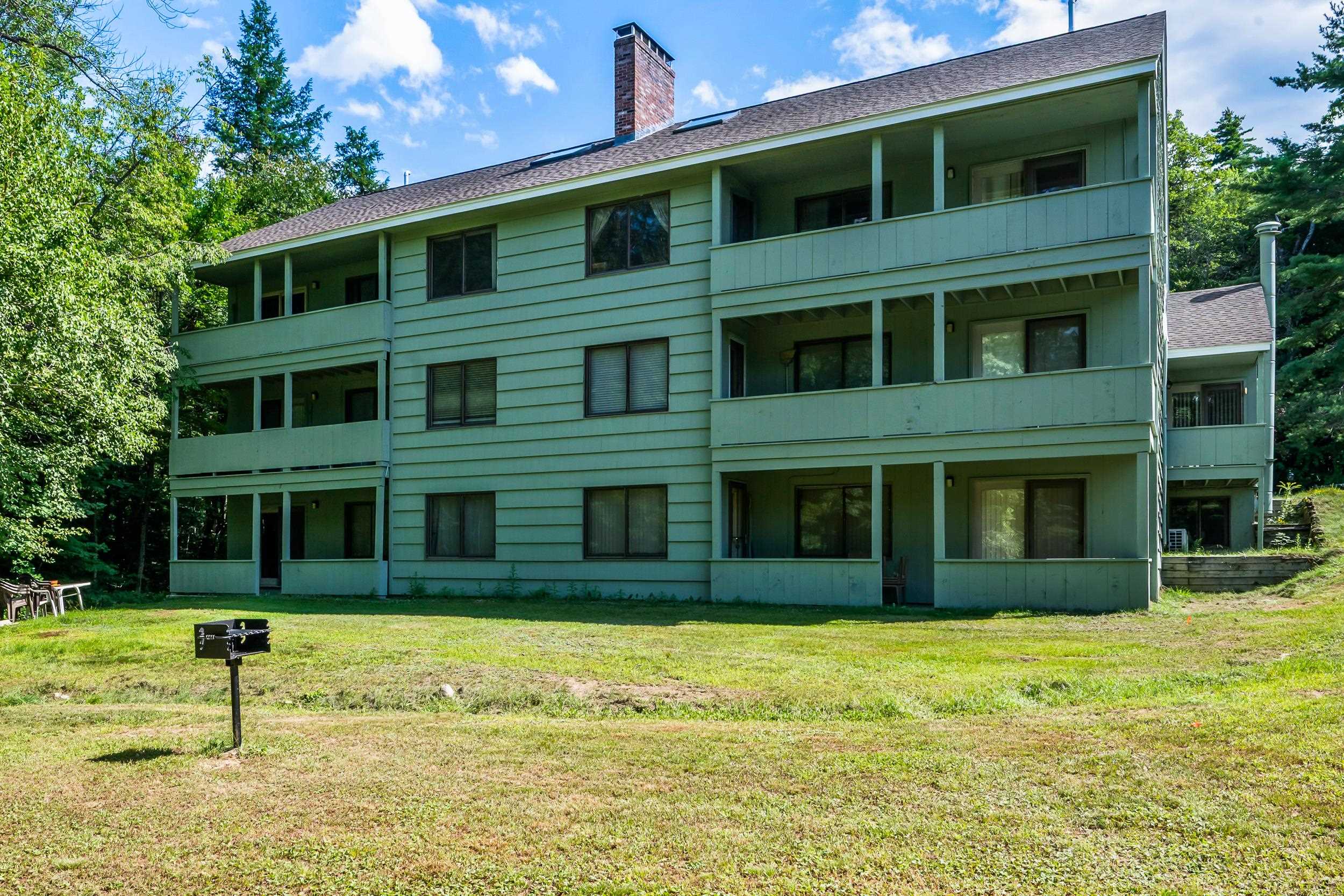 Three-story condominium with covered balconies and a brick chimney, set beside a broad grassy lawn.