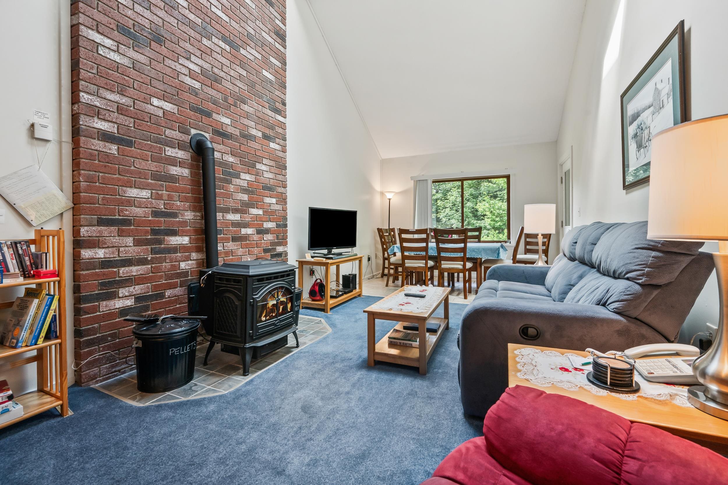 Living room with a brick chimney, pellet stove, blue-gray sofa, and dining area beside a large window.