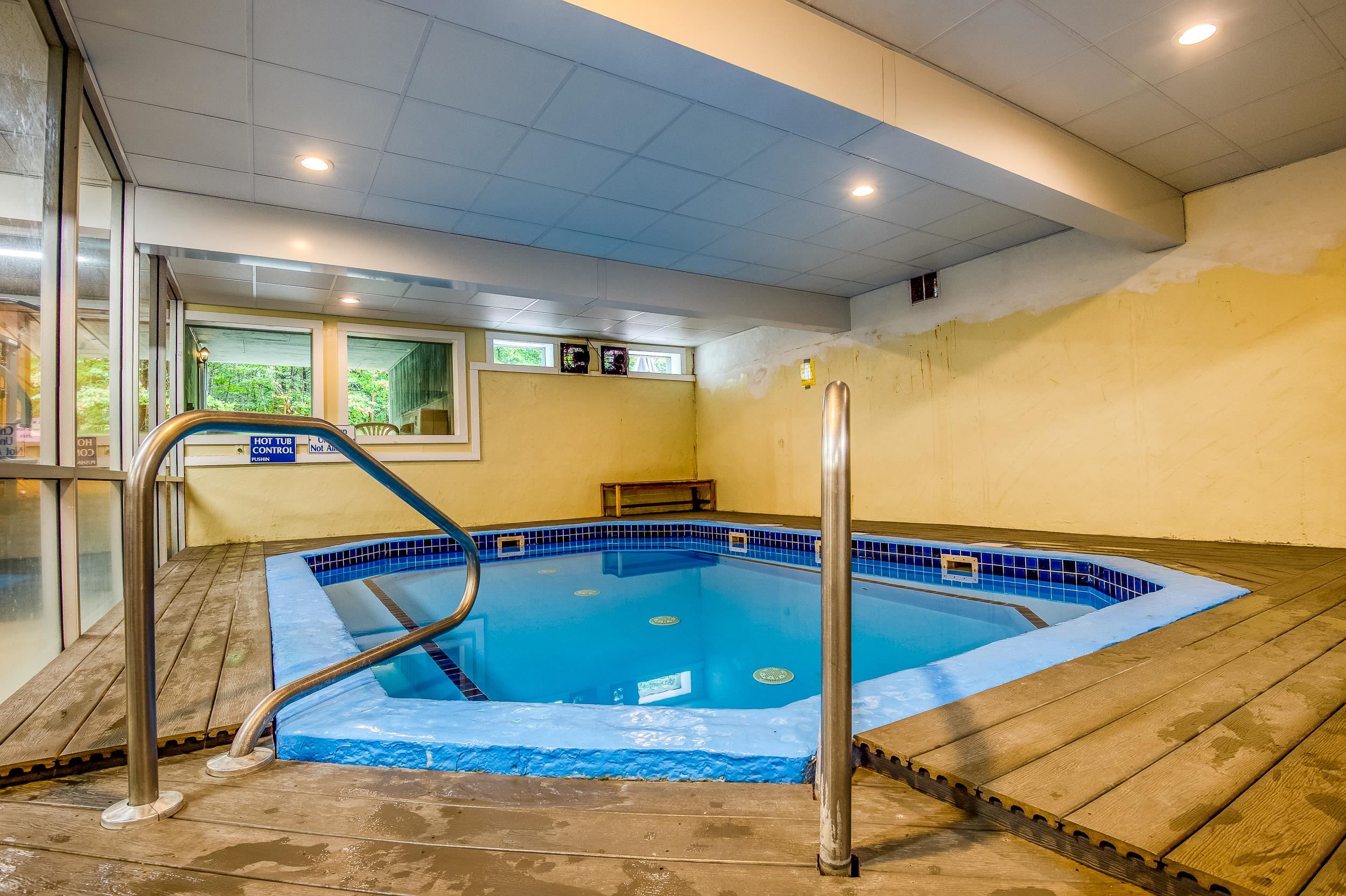 Indoor pool with blue water, tiled edges, stainless-steel handrails, and a wooden deck.