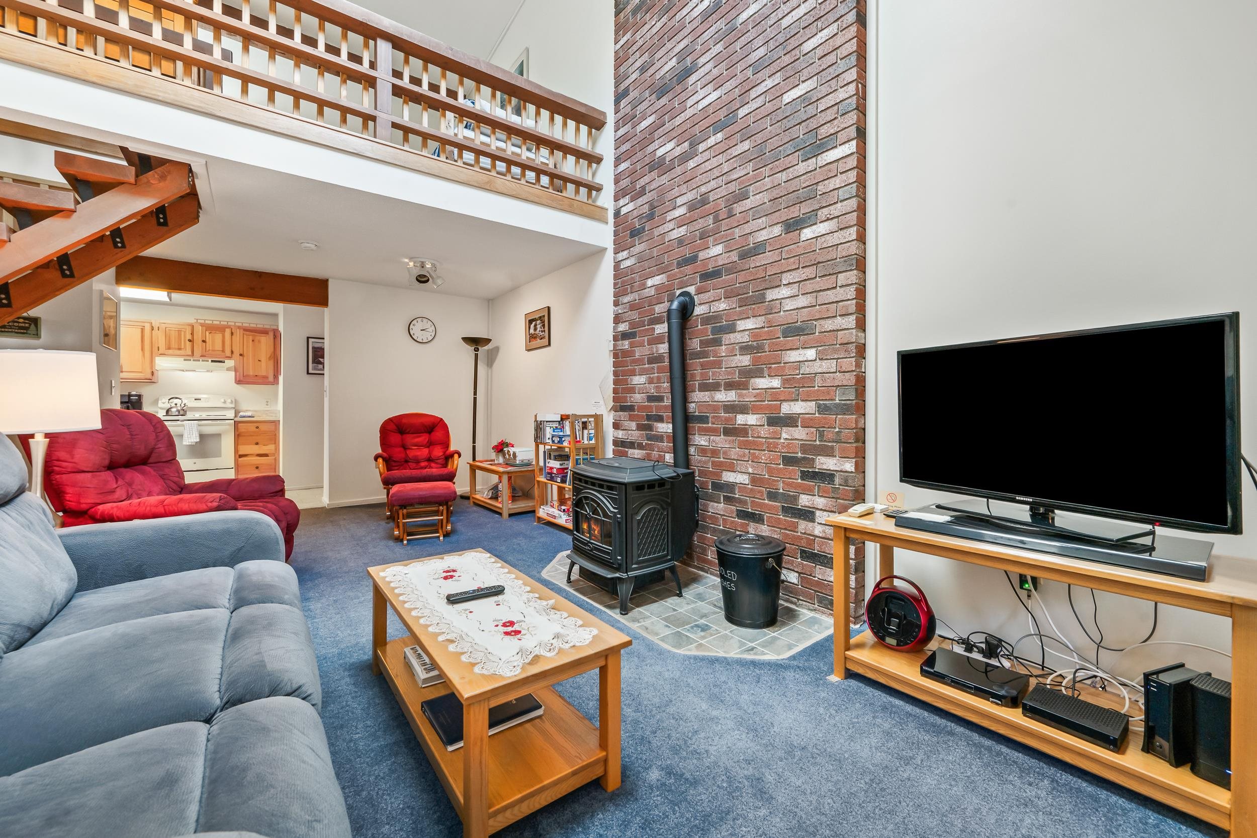 Living room with a brick stove wall, loft railing, blue carpet, and red and blue sofas.