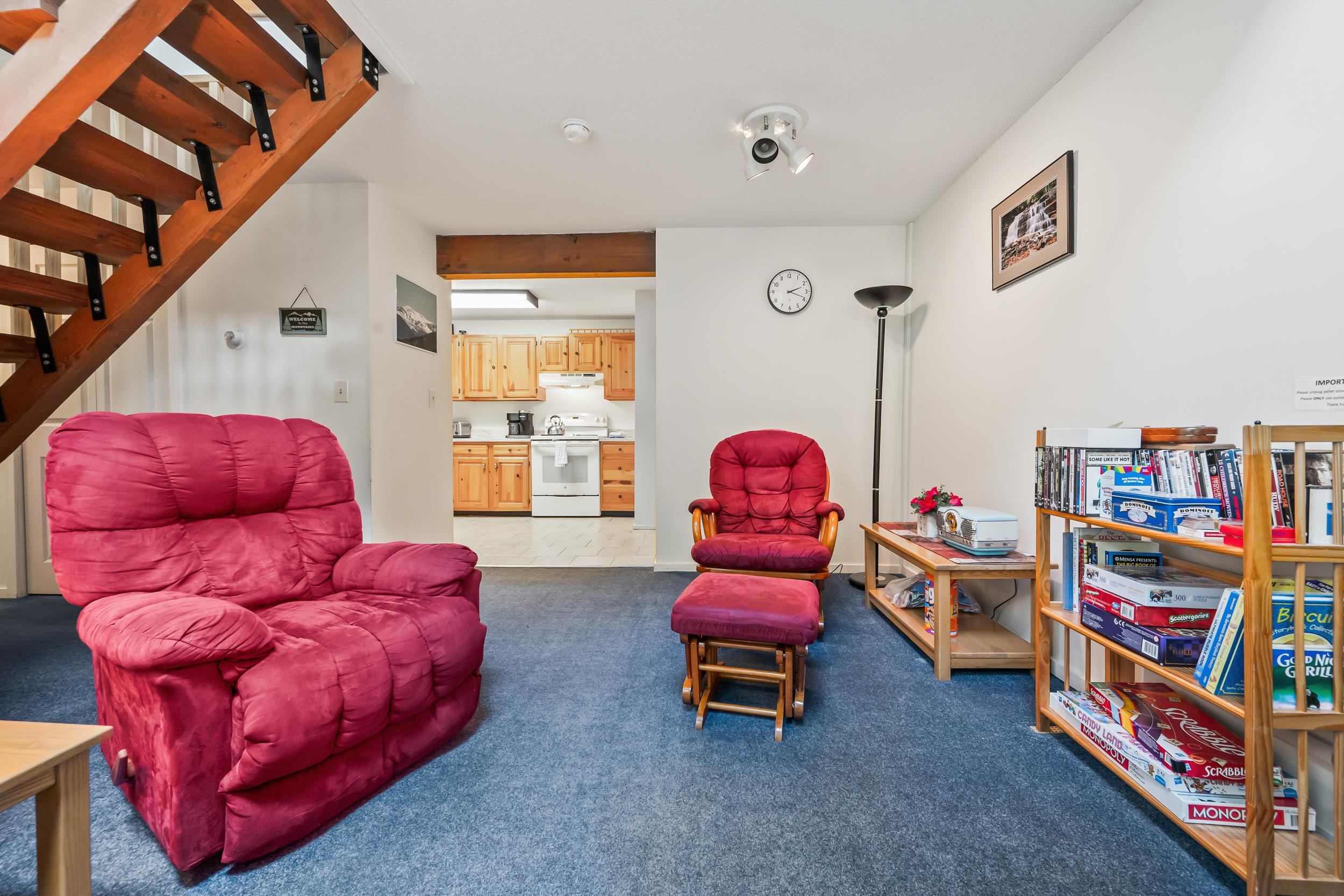 Living room with red recliners, a wooden staircase, and shelves of board games.