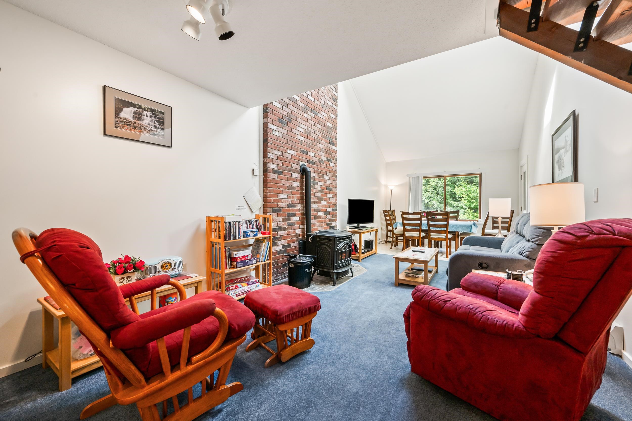Living room with red rocking chairs, a brick fireplace wall, and dining area by a window.