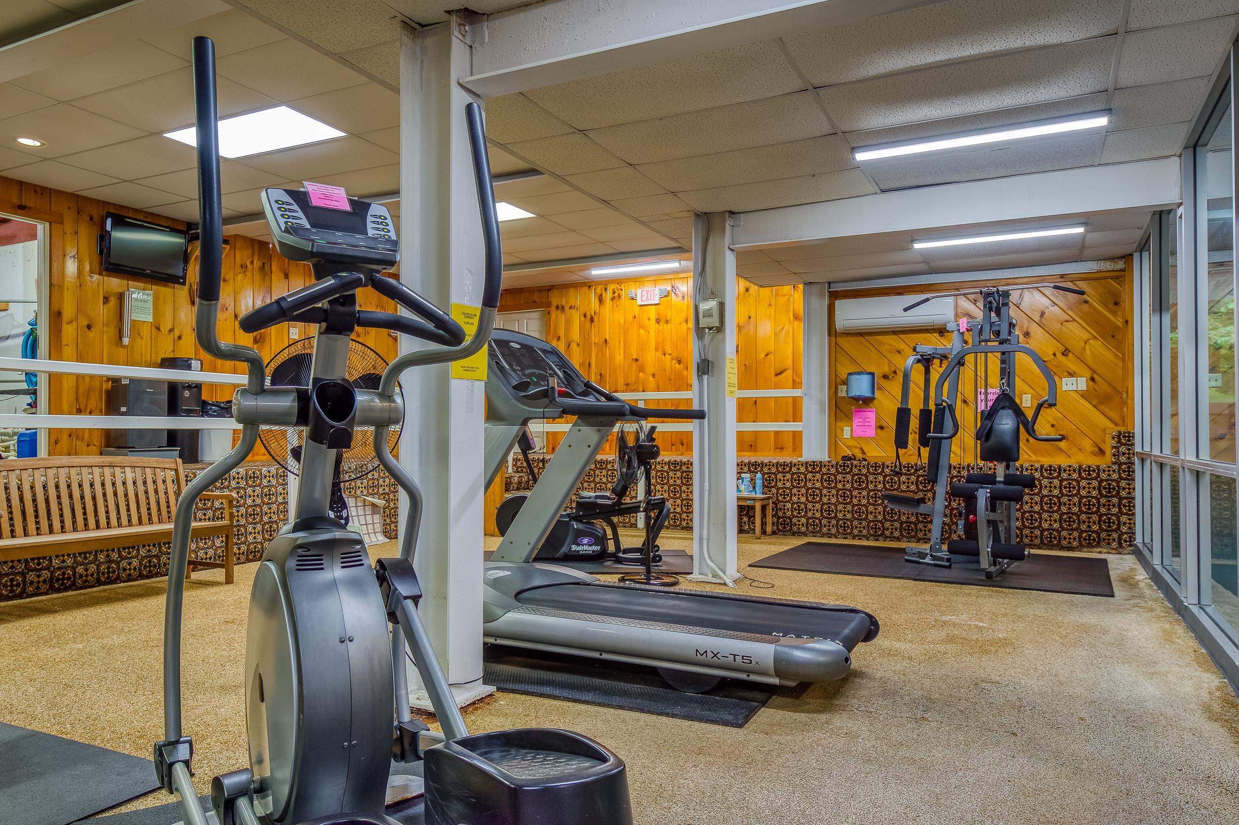 Fitness room with an elliptical, treadmills, weight machine, and wood-paneled walls.