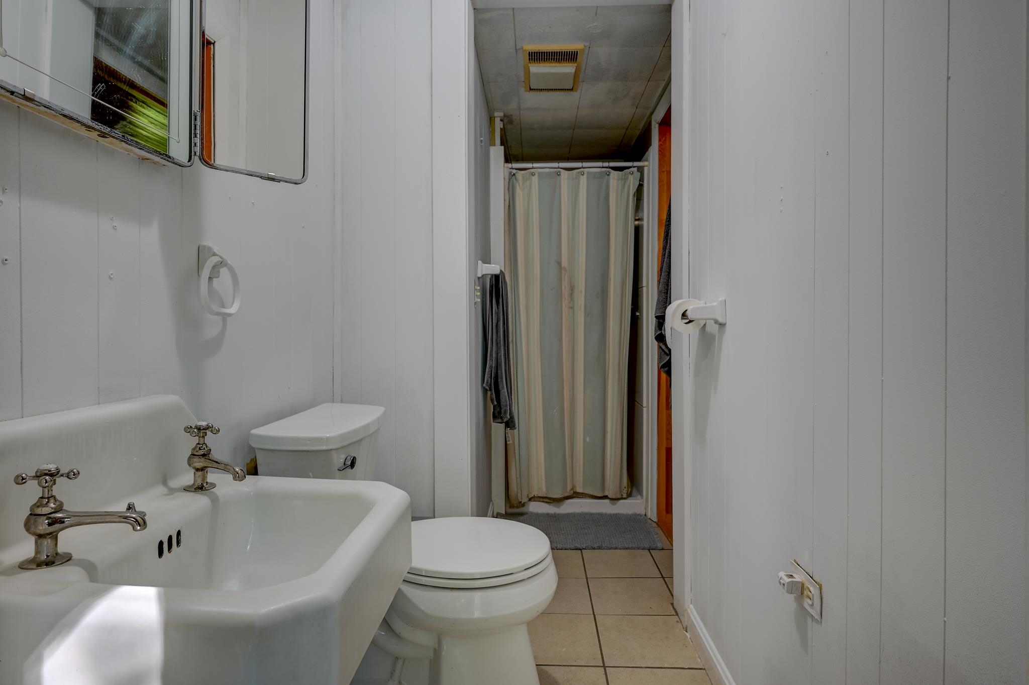 Bathroom with a vintage-style sink, toilet, and curtained shower.