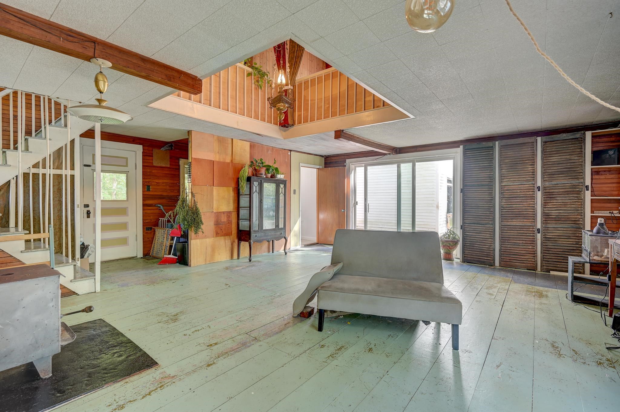 Living room with a gray sofa, open loft railing, staircase, and sliding glass doors.