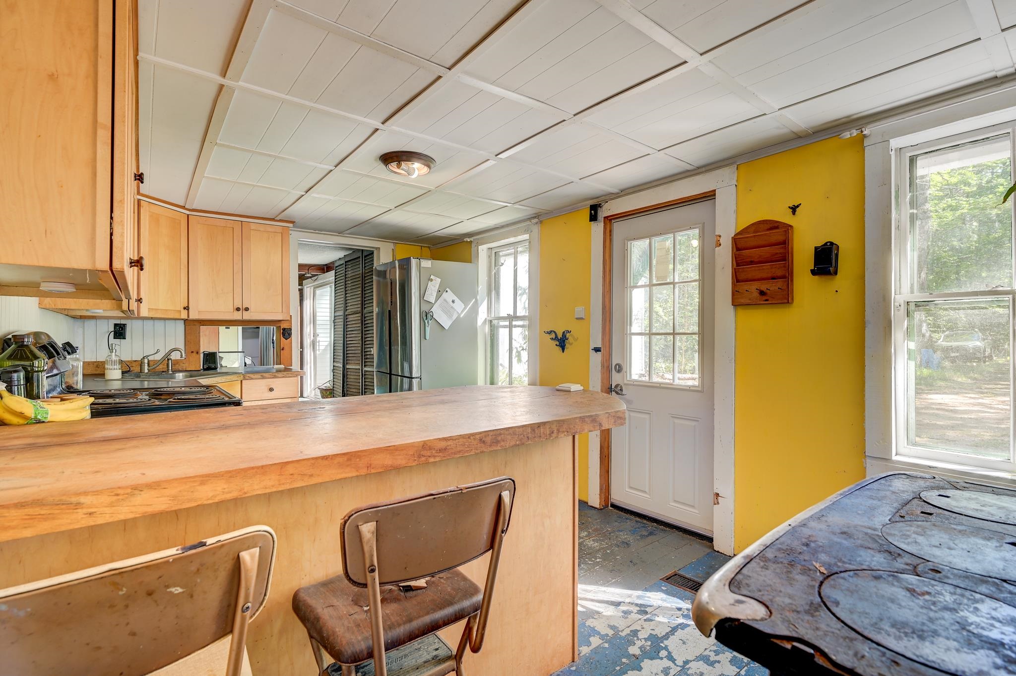 Kitchen with wood cabinets, a broad breakfast bar, yellow wall, and cast-iron cookstove.