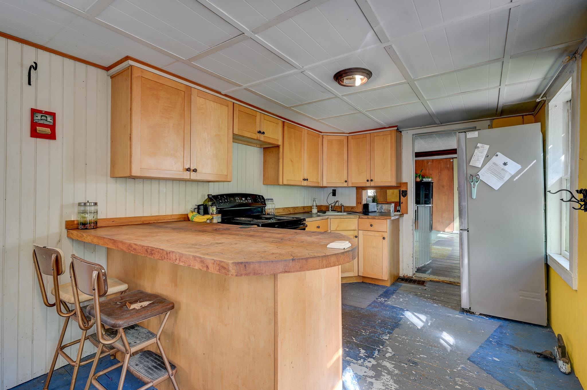 Kitchen with light wood cabinets, a large butcher-block peninsula, bar stools, and a worn blue floor.